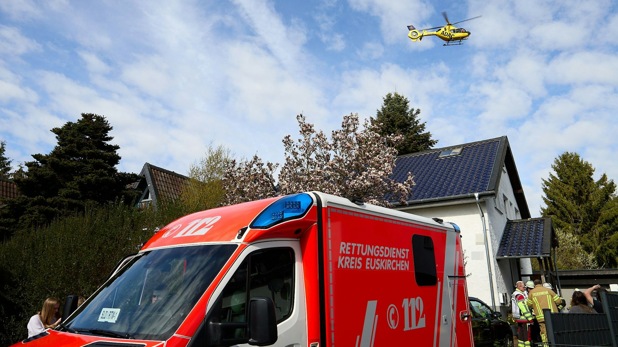Der ADAC-Rettungshubschrauber fliegt über das Haus, davor ein Rettungswagen und Einsatzkräfte.