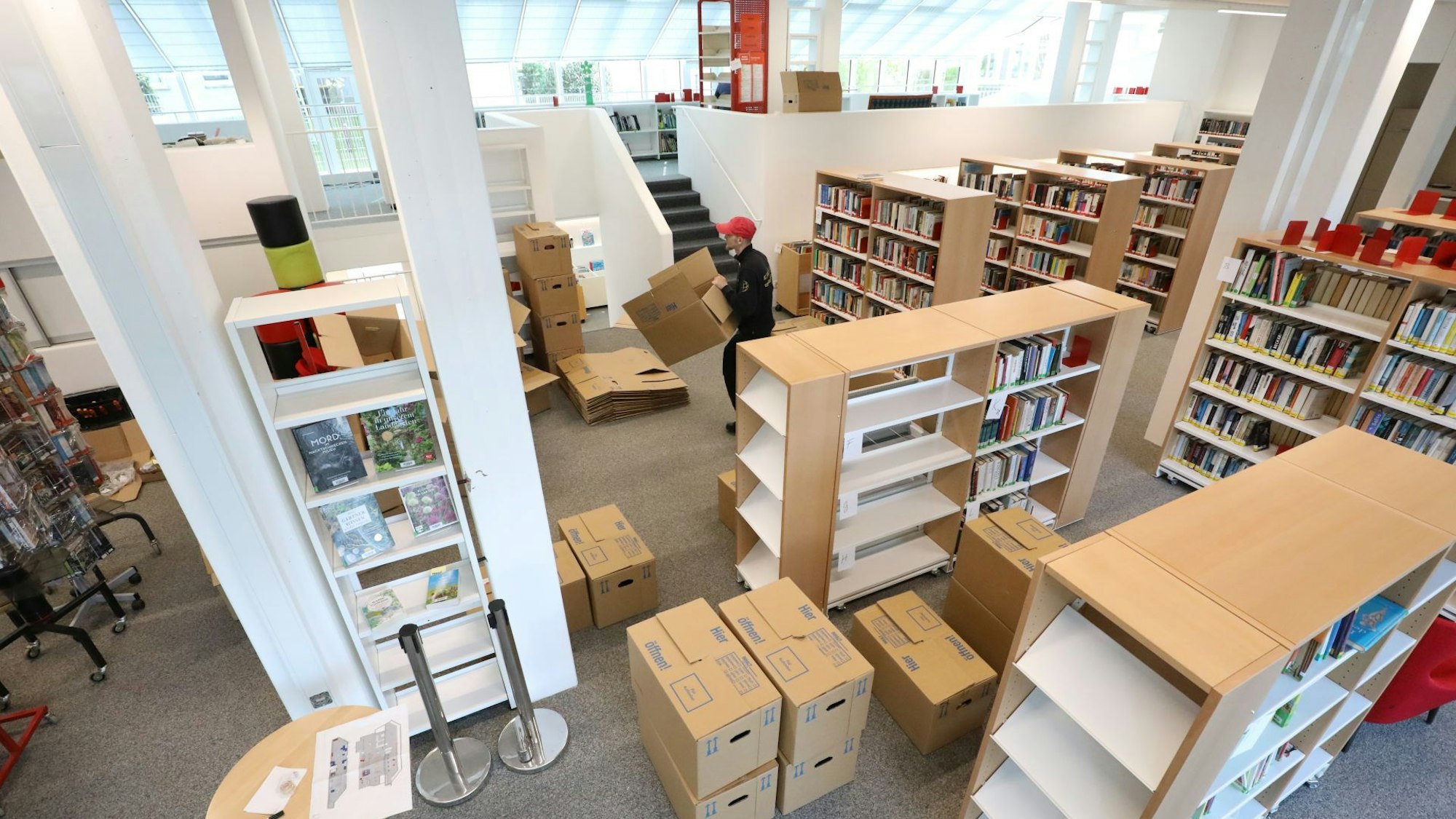 Blick in einen Raum voller Umzugskartons und noch nicht komplett gefüllten Bücherregalen.