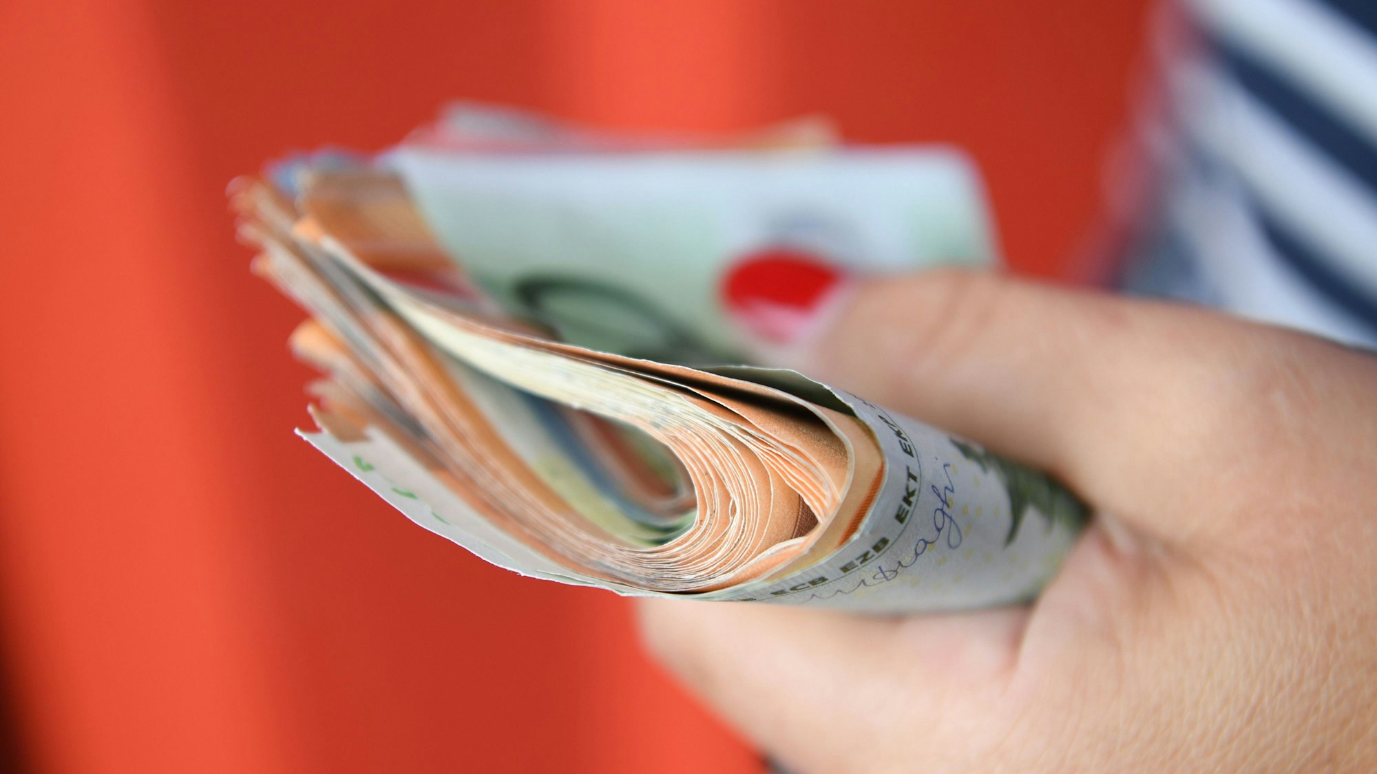 Eine Person hält ein Bündel Geldscheine in der Hand.