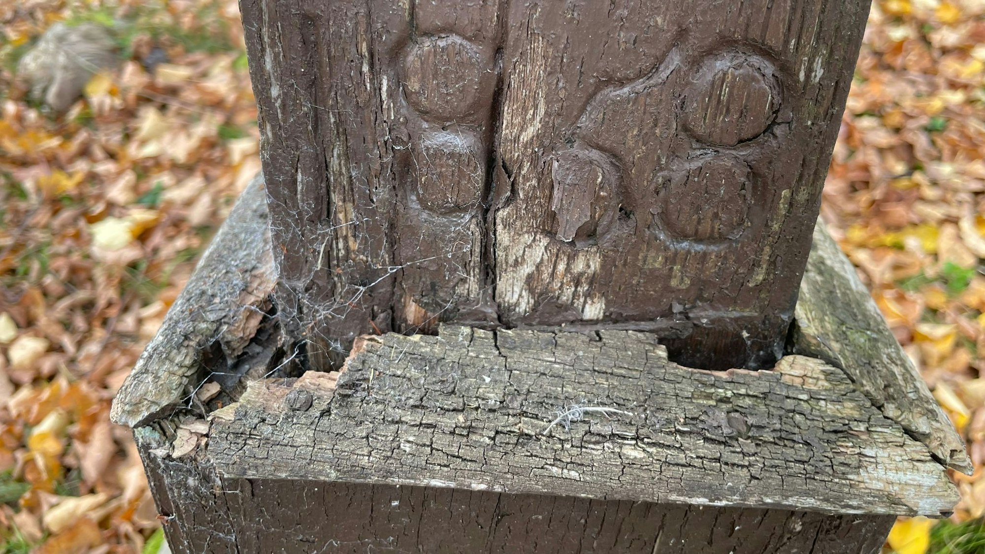 Das Bild zeigt den Sockel, an dem die Farbe abgeblättert und das Holz aufgerissen ist.