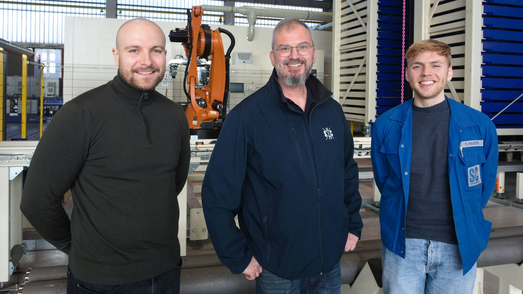 Die drei Männer stehen in einer Halle des Unternehmens.