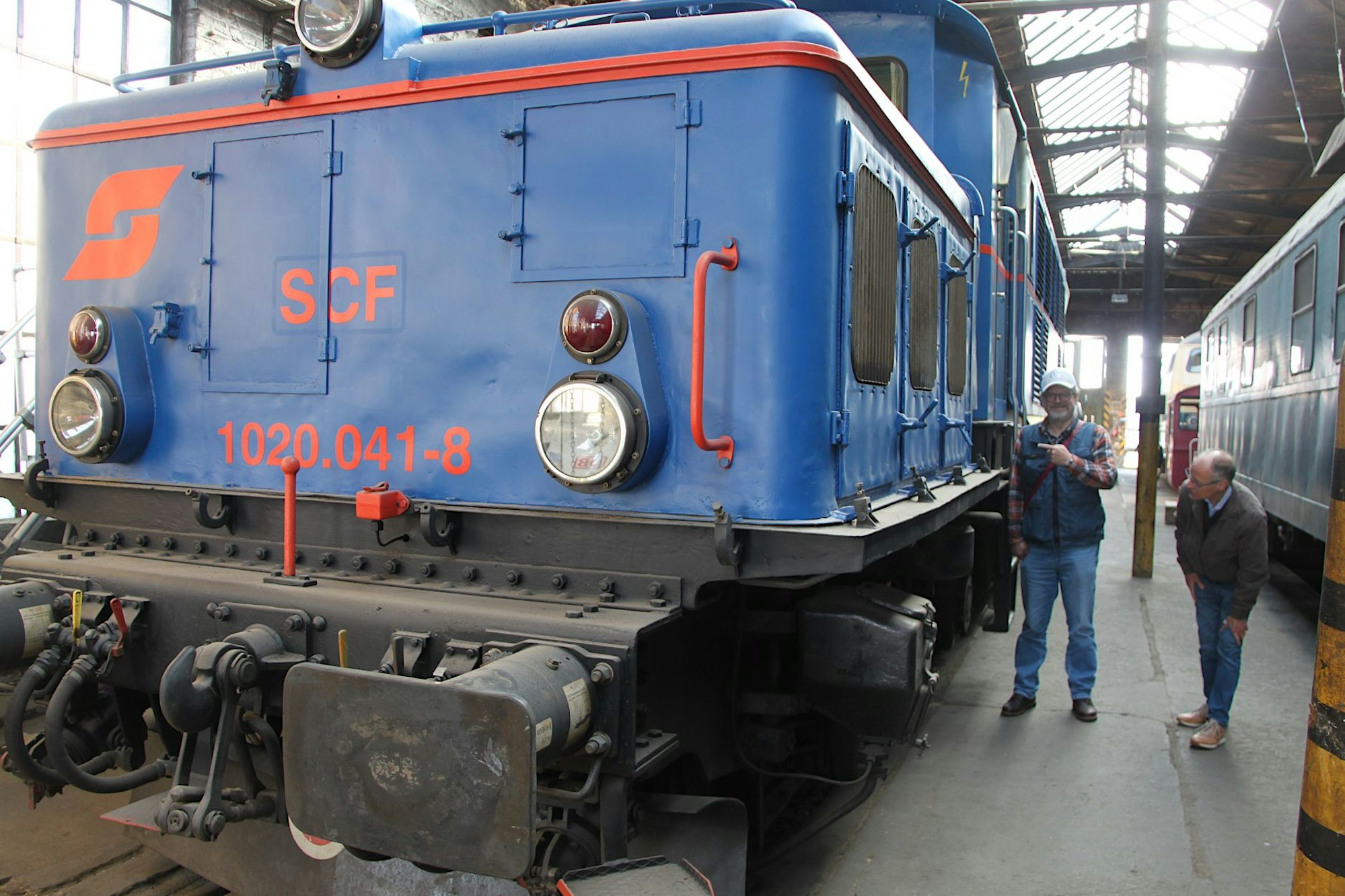 Das Bild zeigt zwei Männer, die neben einer großen blauen Lok stehen.