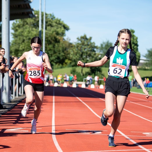 Das Bild zeigt zwei Nachwuchsläuferinnen, während sie die Ziellinie überqueren.