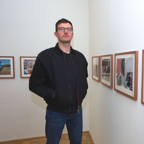 Ein junger Mann steht vor gerahmten Fotografien.