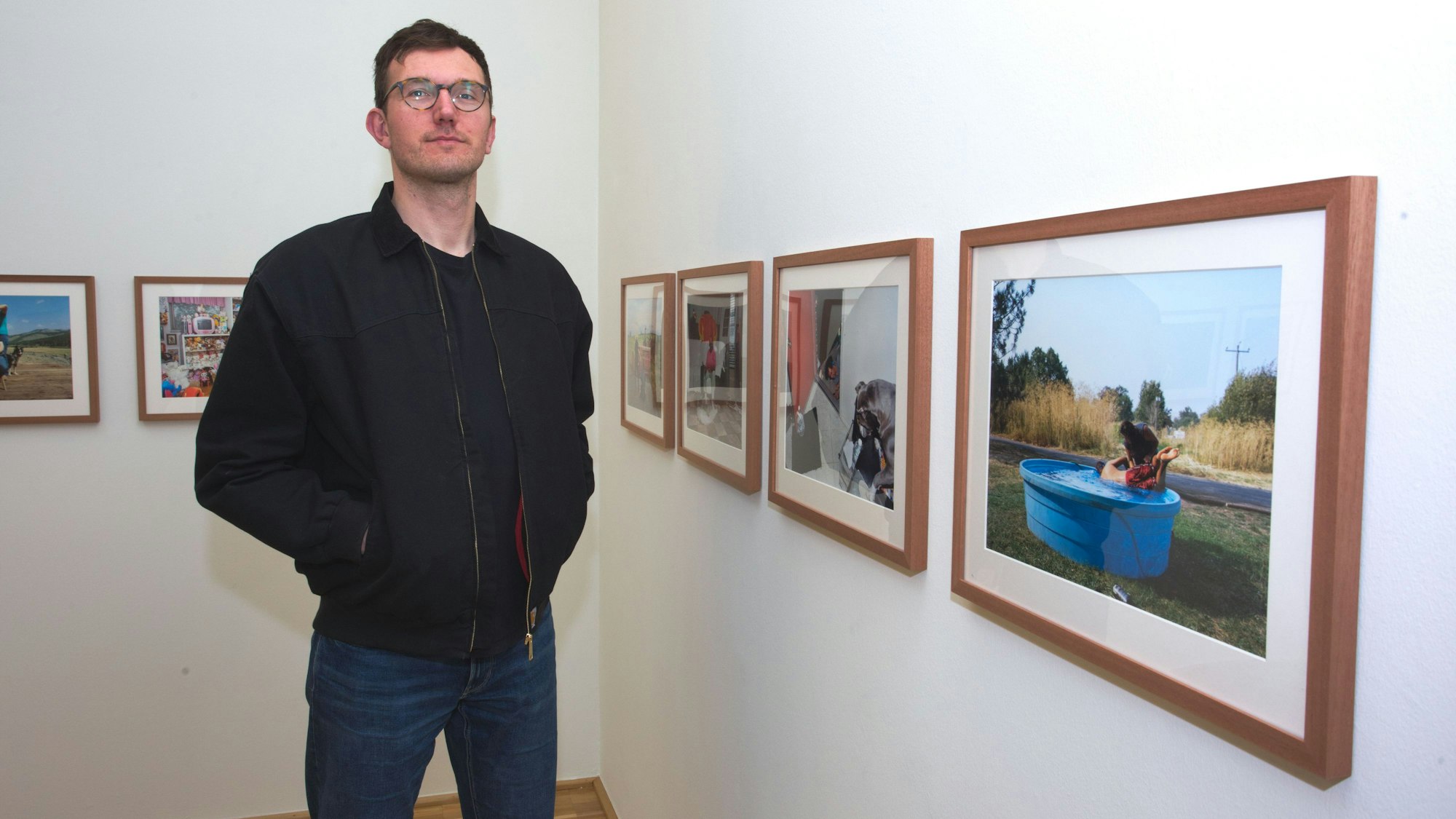 Ein junger Mann steht vor gerahmten Fotografien.