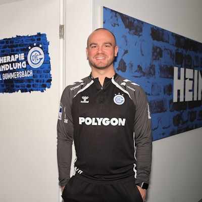 Ein Mann steht vor einer Kabine, anderen Tür die Aufschrift „Physiotherapie“ zu lesen ist.