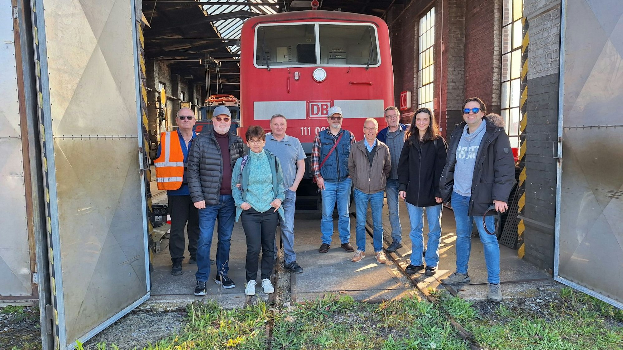 Eine Gruppe Menschen steht vor einer roten Eisenbahn-Lok.