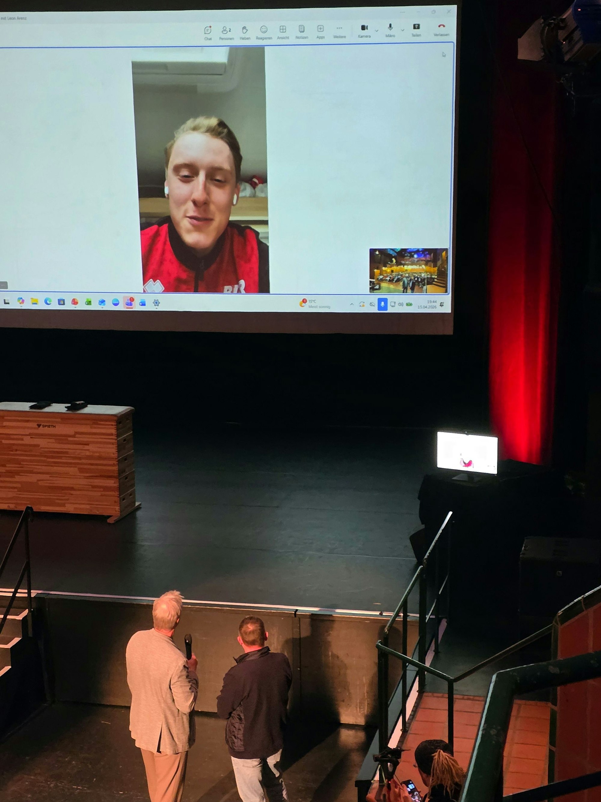 Menschen stehen im Bergischen Löwen vor einer Videoleinwand mit Videoschaltung.