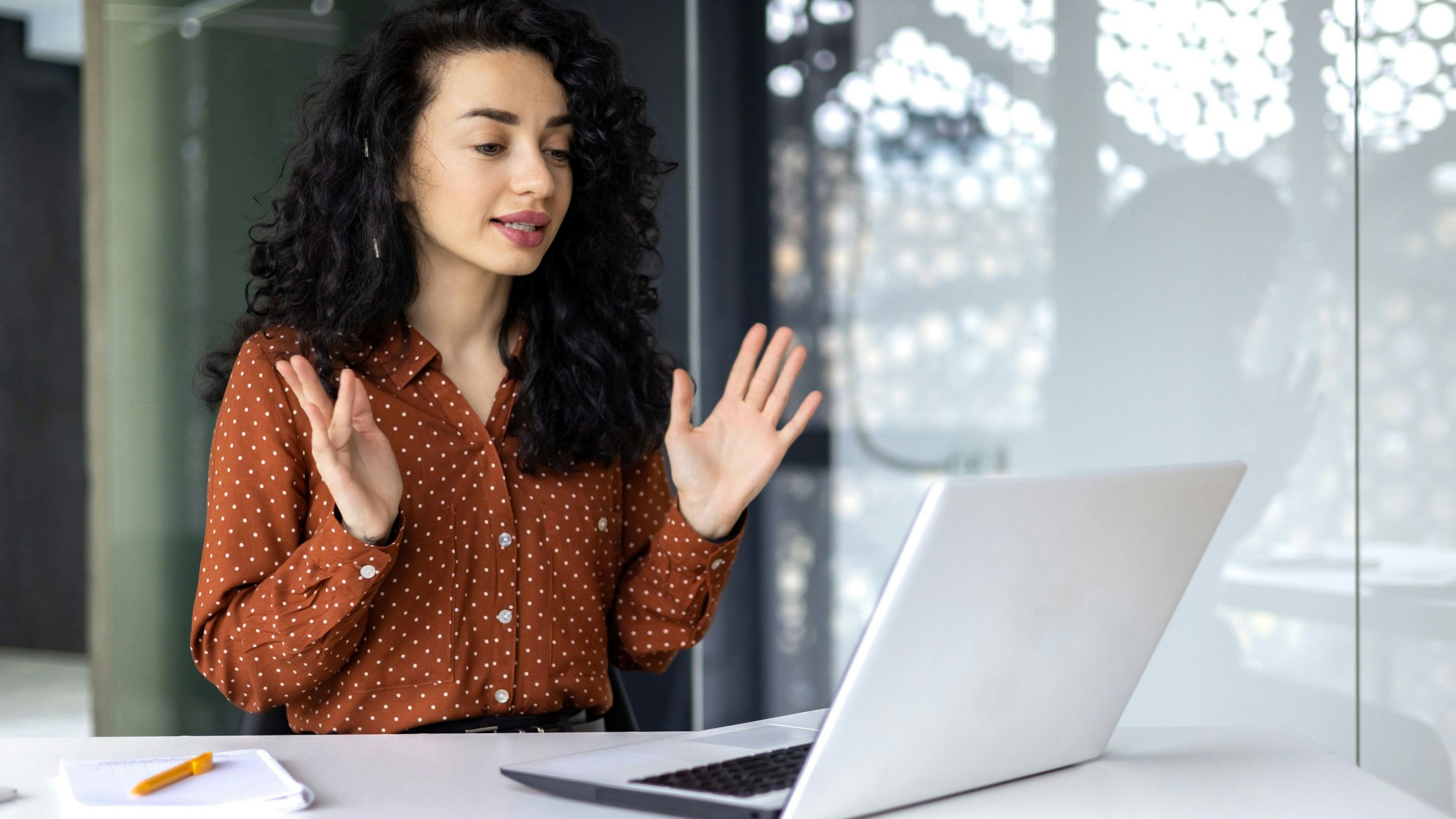 Eine junge Frau mit Headset nimmt an einem Video-call teil. Vor ihr steht ein aufgeklappter Laptop.