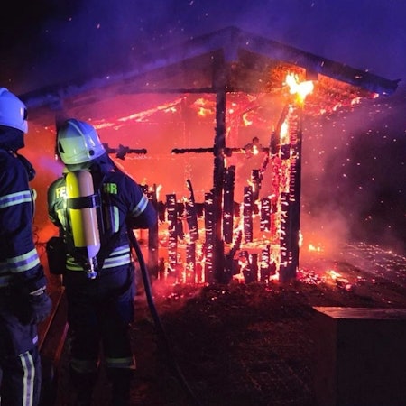 Feuerwehrleute löschen ein Holzhaus, das in voller Ausdehnung brennt.