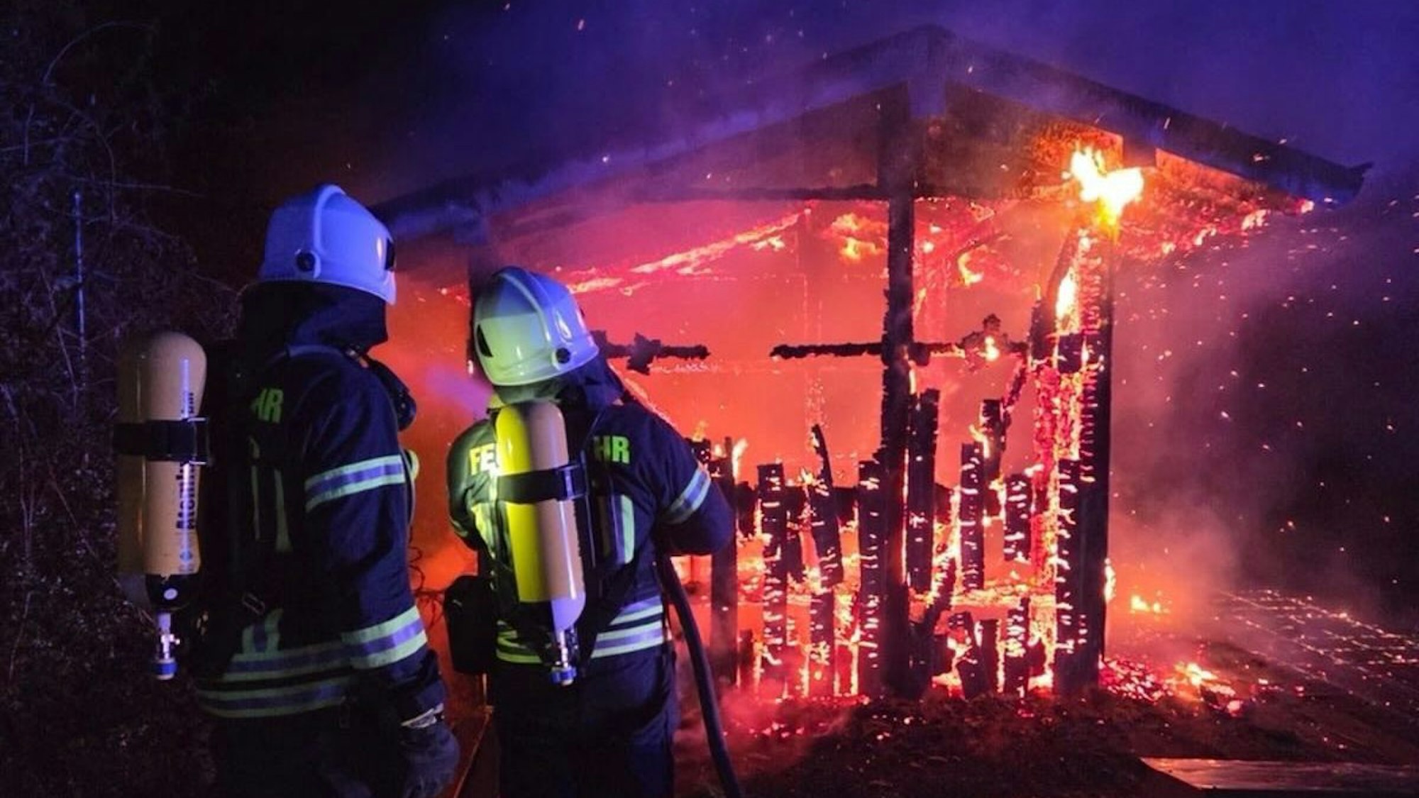 Feuerwehrleute löschen ein Holzhaus, das in voller Ausdehnung brennt.