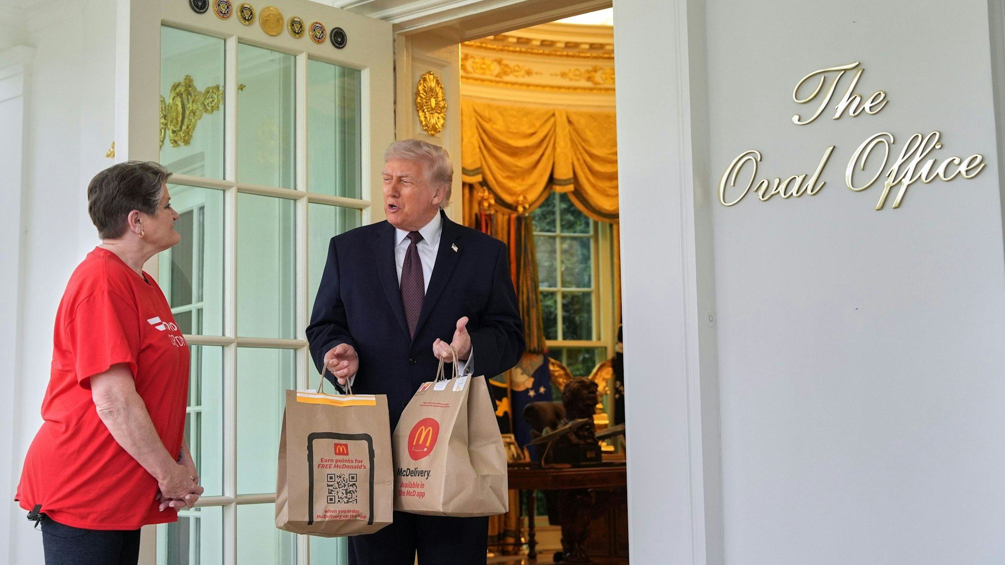 13.04.2026, USA, Washington: US-Präsident Donald Trump spricht mit einer Frau von Door Dash, die ihm zwei Tüten mit McDonald's-Essen zum Oval Office des Weißen Hauses geliefert hat. Foto: Alex Brandon/AP/dpa +++ dpa-Bildfunk +++