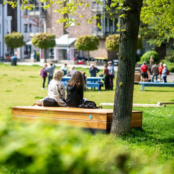 Das Bild zeigt einen Blick in den Klostergarten. Auf einer Sitzgelegenheit aus Holz haben zwei Frauen Platz genommen.