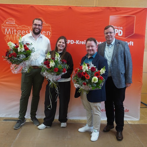 Das Bild zeigt die Kandidaten mit Herrwegen vor einem SPD-Banner. Die Kandidaten halten Blumensträuße.
