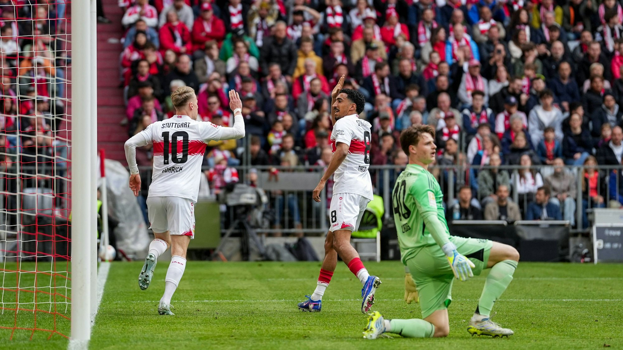 Bayern-Keeper Jonas Urbig reagiert nach dem 0:1 gegen den VfB, Chris Führich dreht jubelnd ab.
