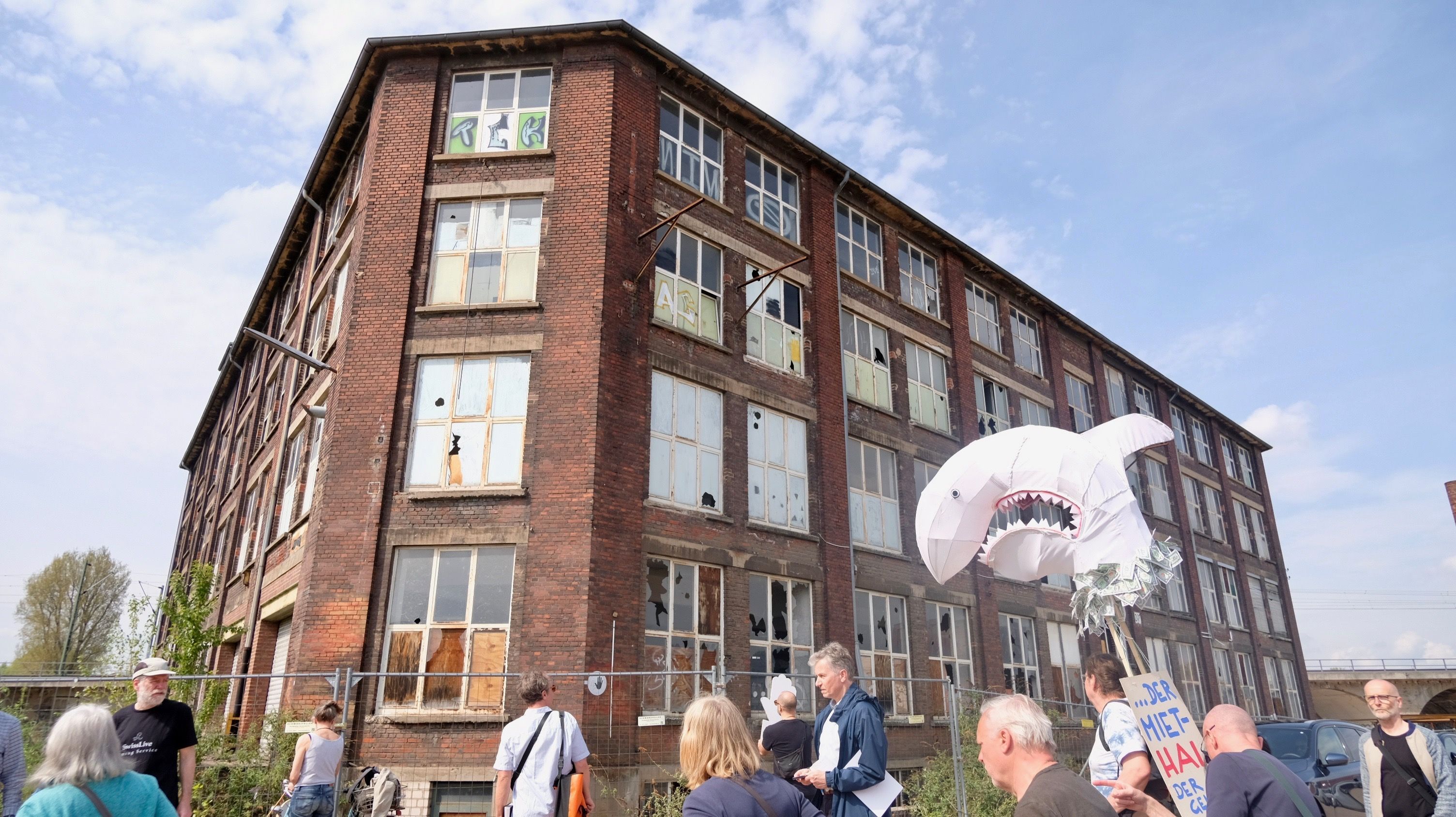 Demonstranten mit einem Miethai aus Pappe ziehen vor einer Ruine entlang.
