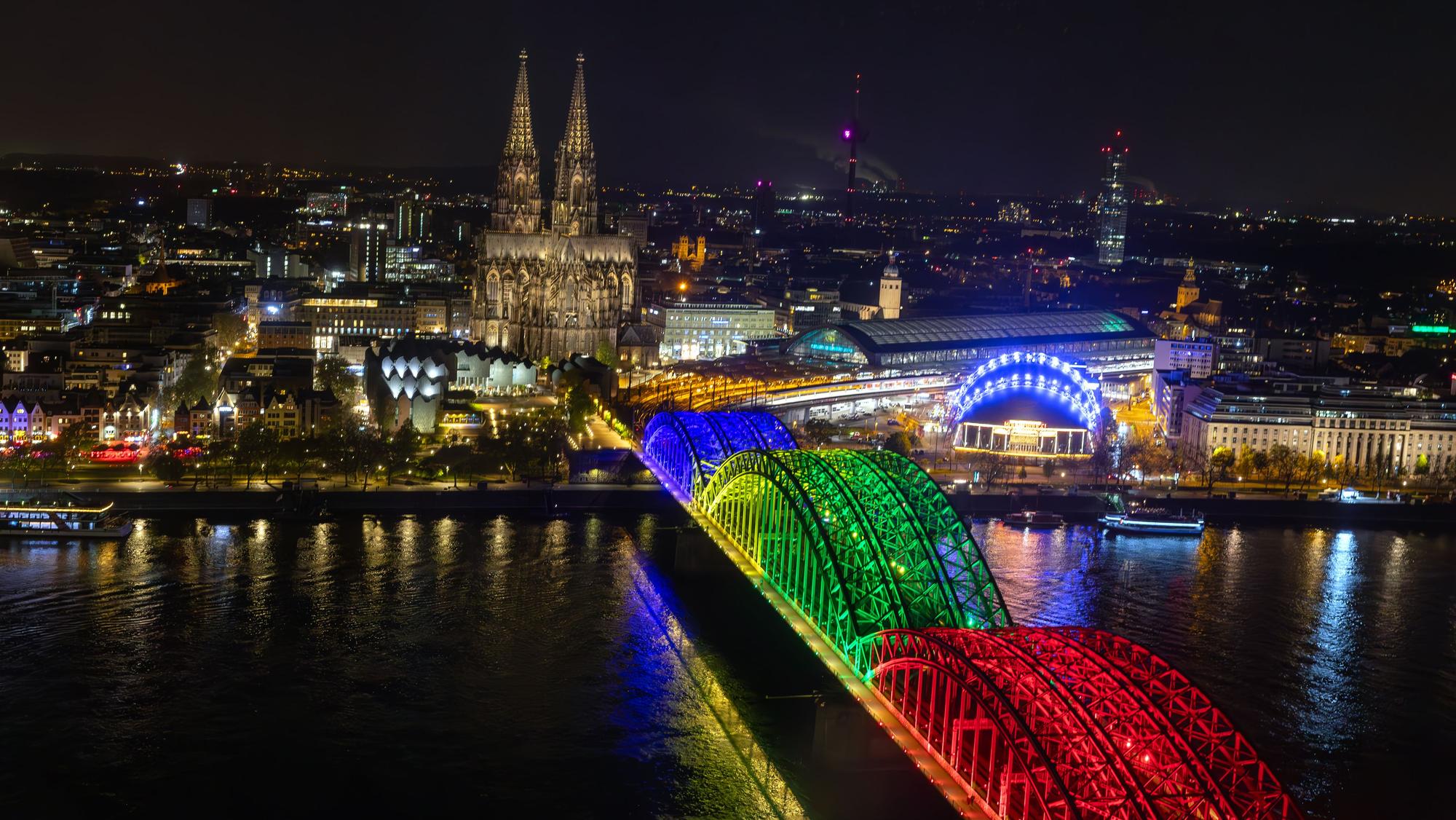 Die Bögen der Hohenzollernbrücke bunt beleuchtet in den Farben der olympischen Ringe.