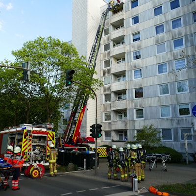 Feuerwehrleute stehen Einsatzwagen und Drehleiter vor einem Hochhaus in Meckenheim.