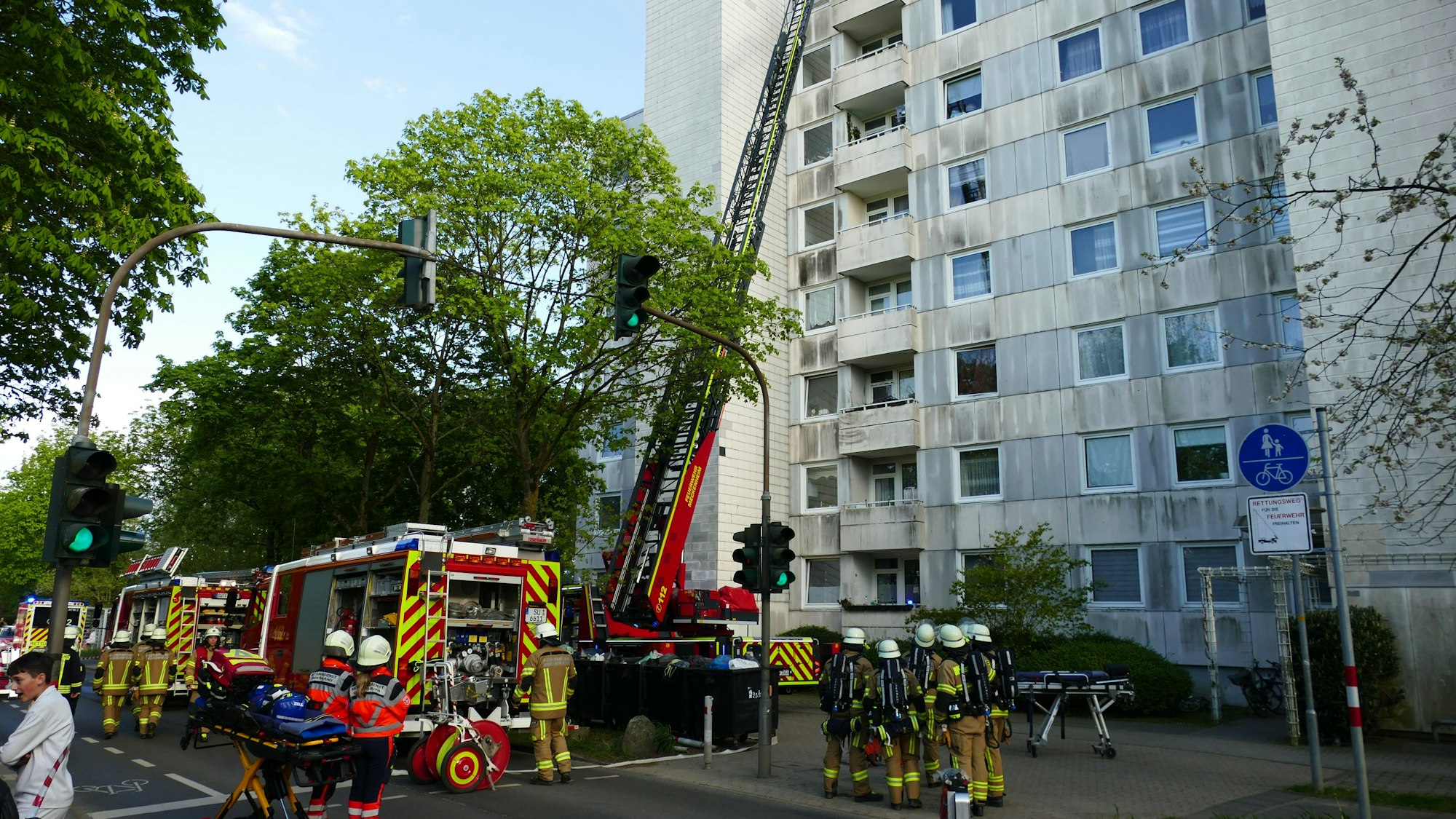 Feuerwehrleute stehen Einsatzwagen und Drehleiter vor einem Hochhaus in Meckenheim.