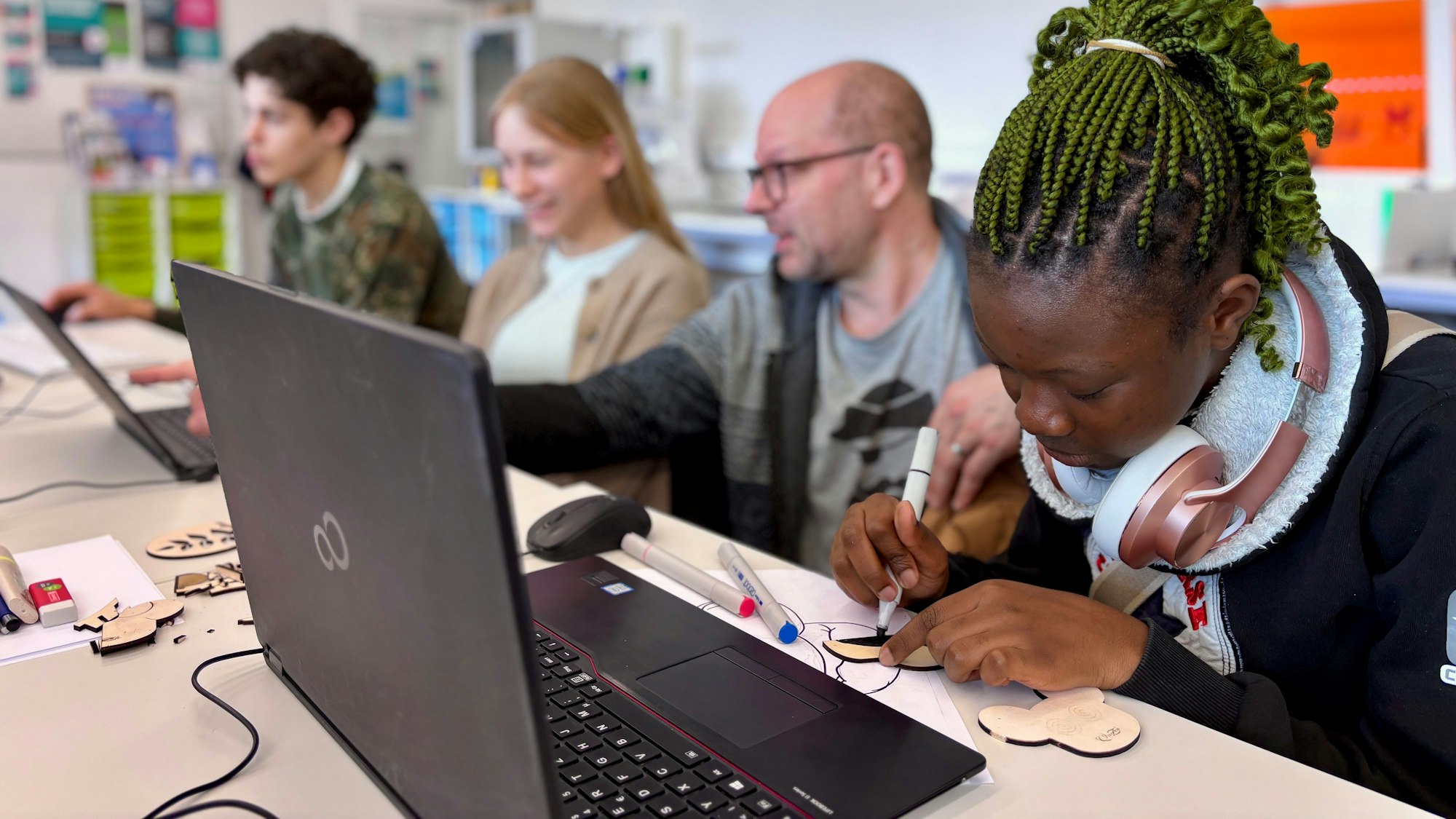 Eine Jugendliche gestaltet ein Logo auf einem Blatt Papier mit Markern.