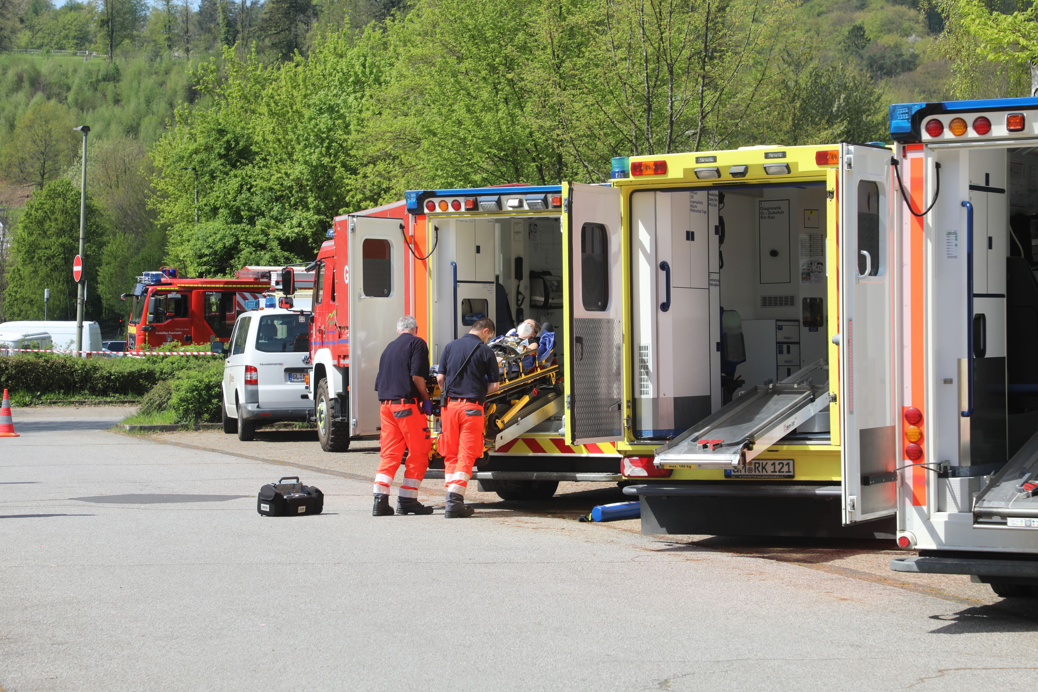 Rettungsassistenten schieben eine Trage mit einem Patienten in einen von mehreren nebeneinander stehenden Rettungswagen.