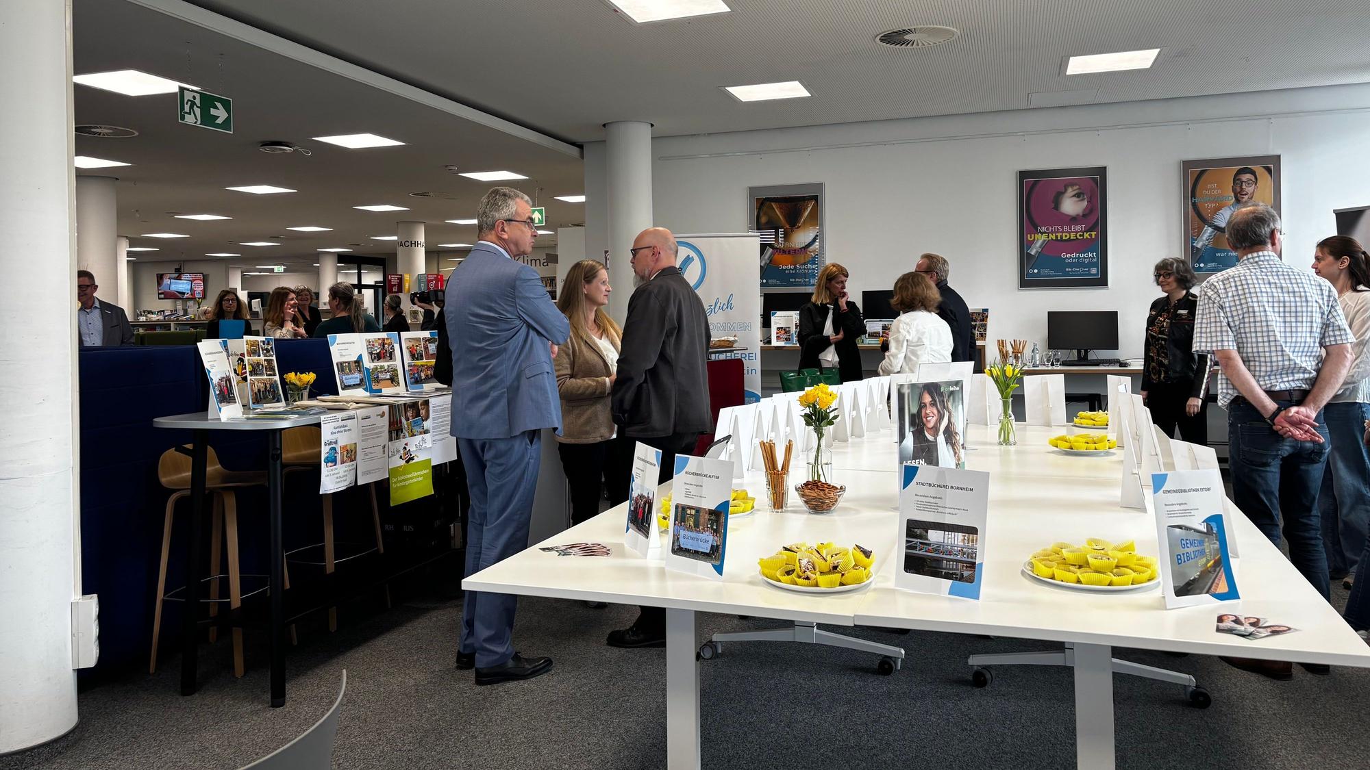Blick in den Raum. Menschen stehen um die Stände der Bibliotheken verteilt.