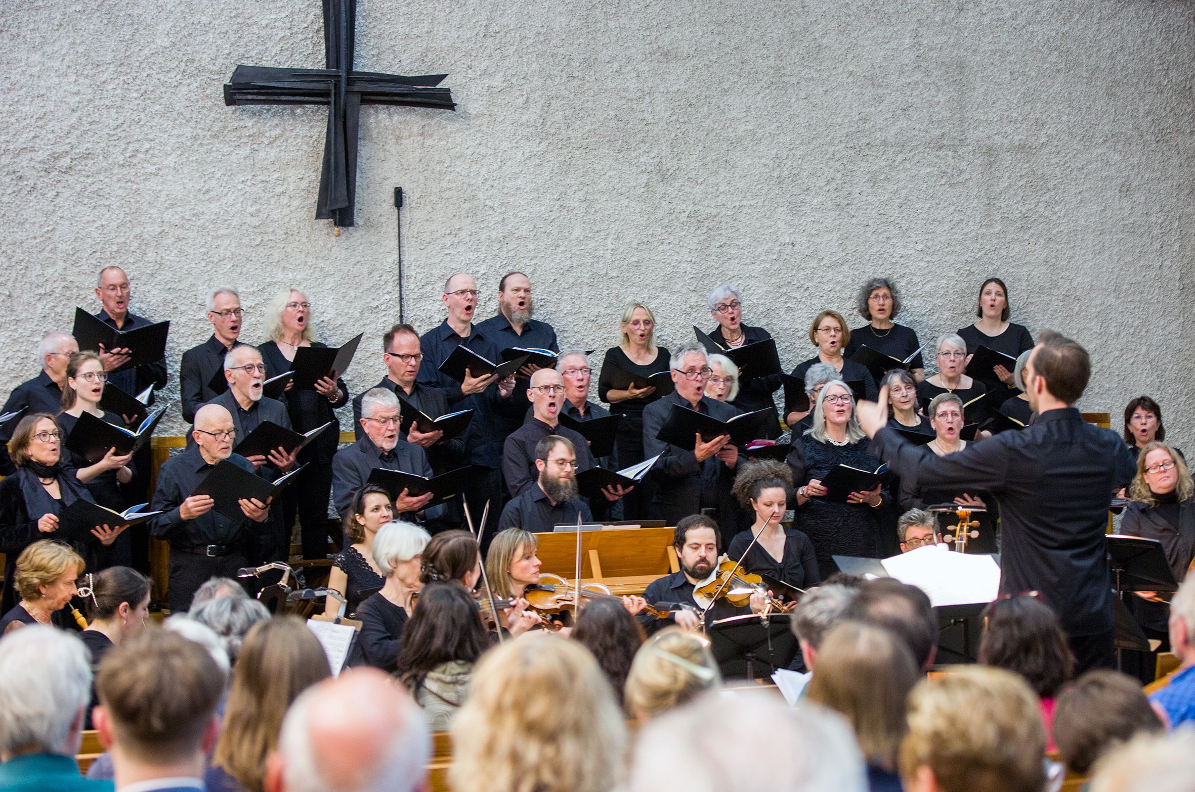 Etwa 40 Sängerinnen und Sänger in schwarzen Hemden singt, dirigiert von einem jungen Mann.