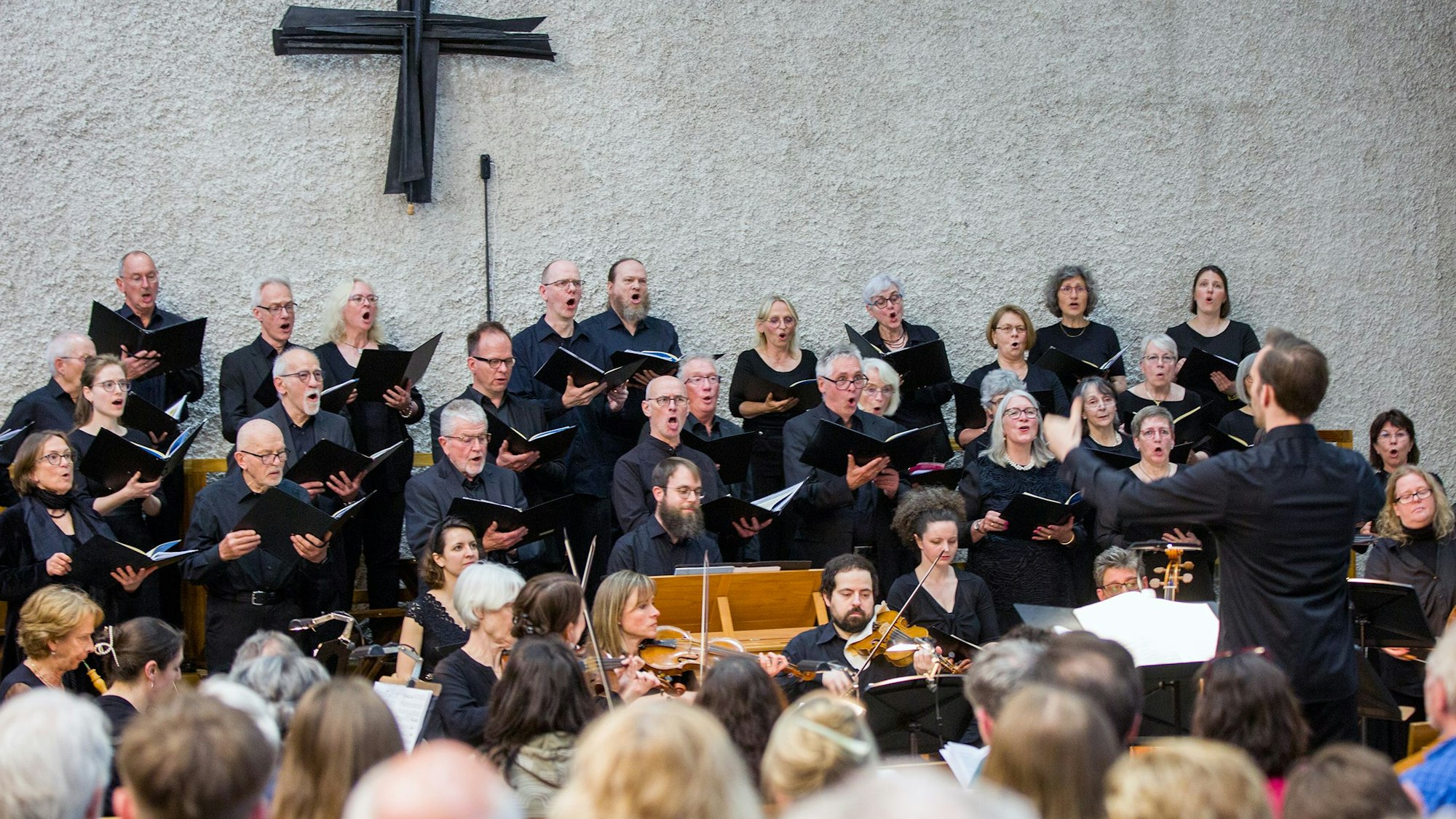 Etwa 40 Sängerinnen und Sänger in schwarzen Hemden singt, dirigiert von einem jungen Mann.