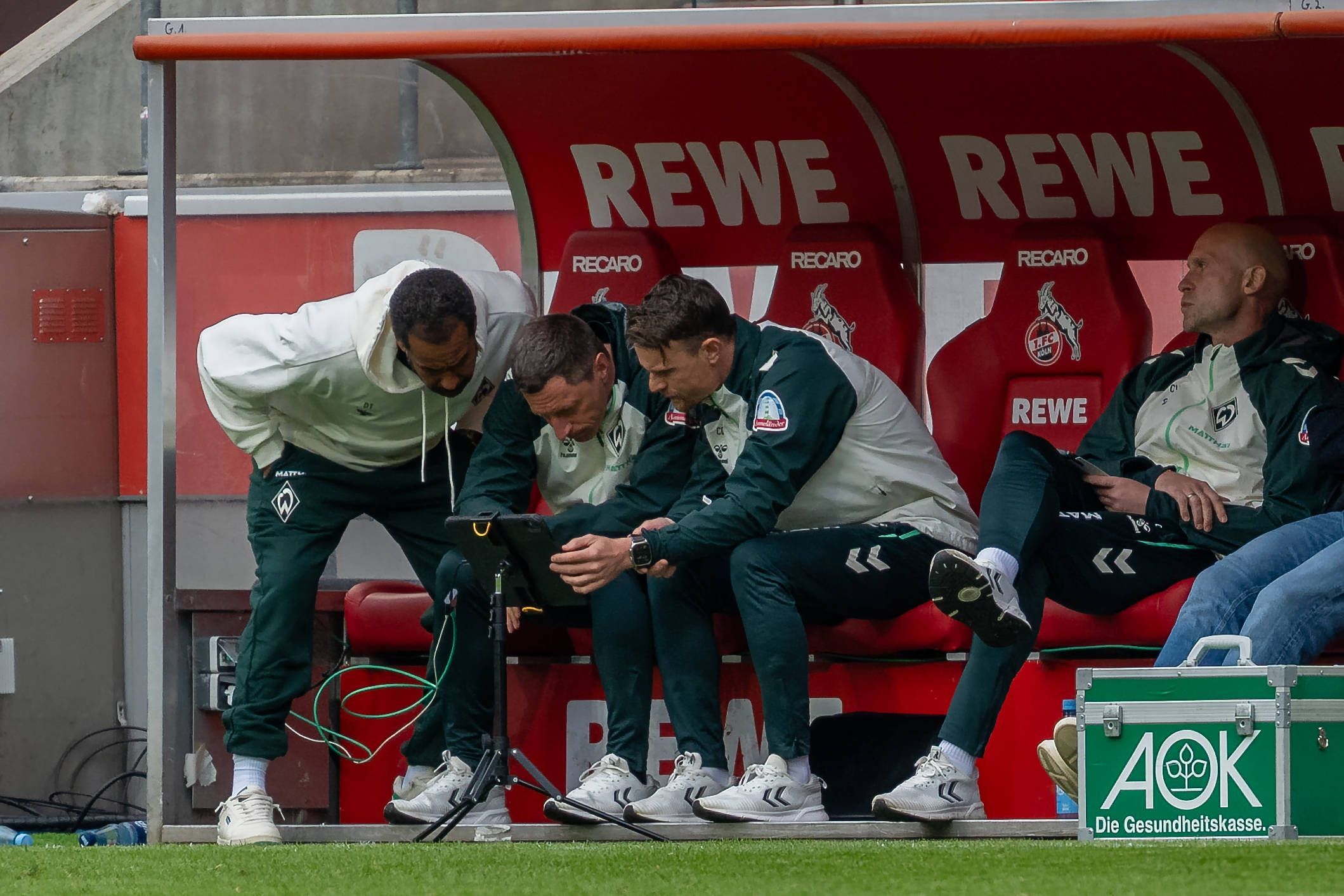 Bei einer Spielunterbrechung riskiert auch Trainer Daniel Thioune (l.) von Werder Bremen einen Blick auf das Tablet vor seiner Trainerbank.