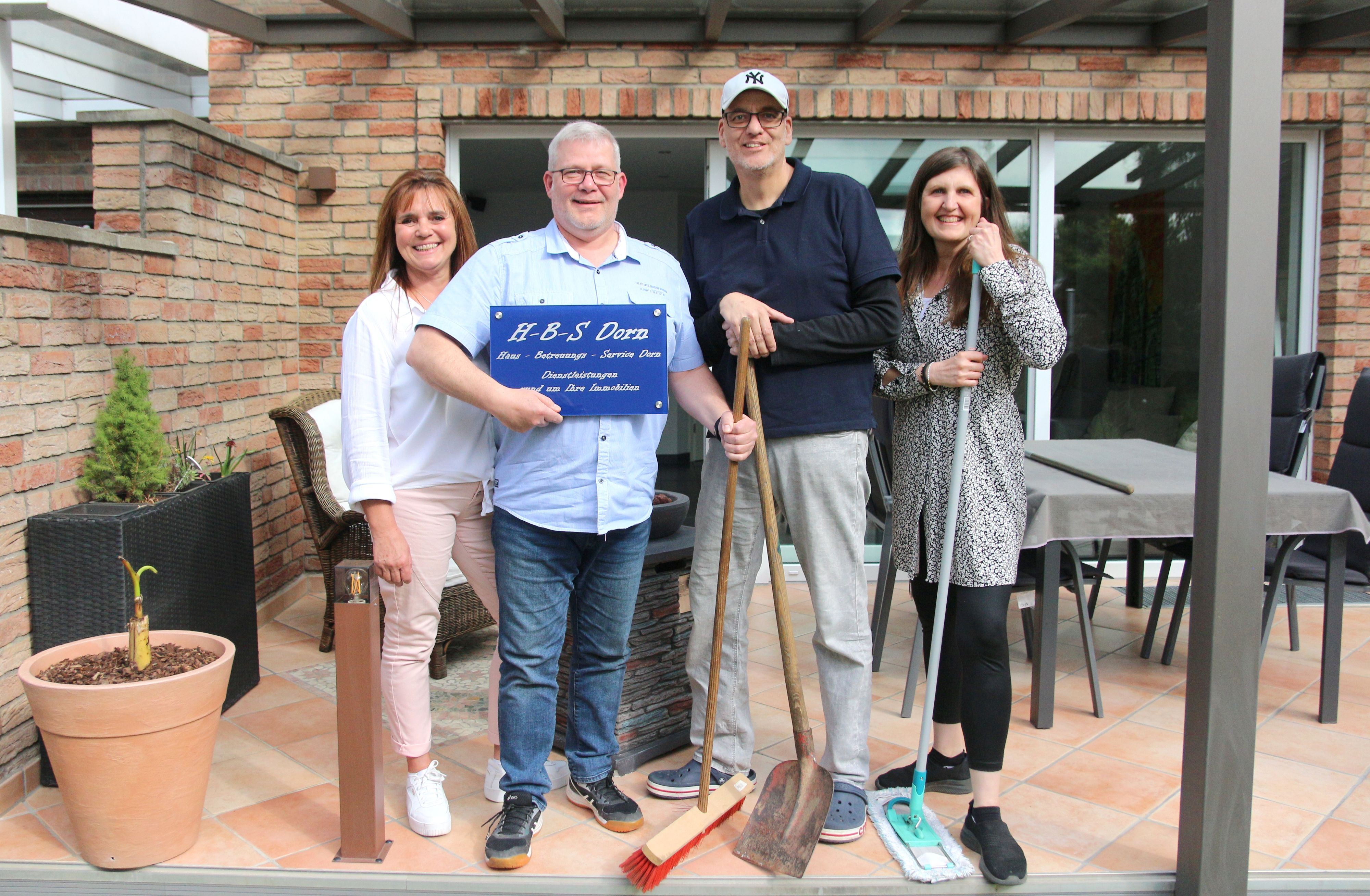 Zwei Männer und zwei Frauen lächeln in die Kamera, einer hält ein Firmenschild im Arm.