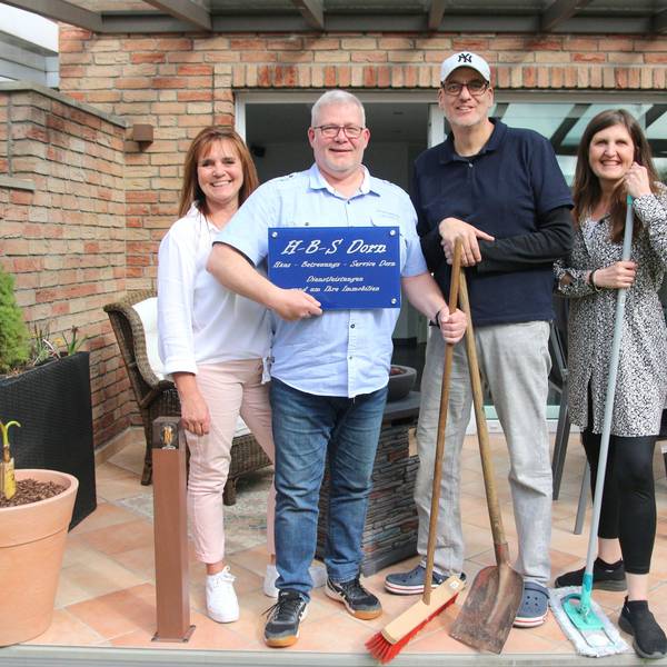 Zwei Männer und zwei Frauen lächeln in die Kamera, einer hält ein Firmenschild im Arm.