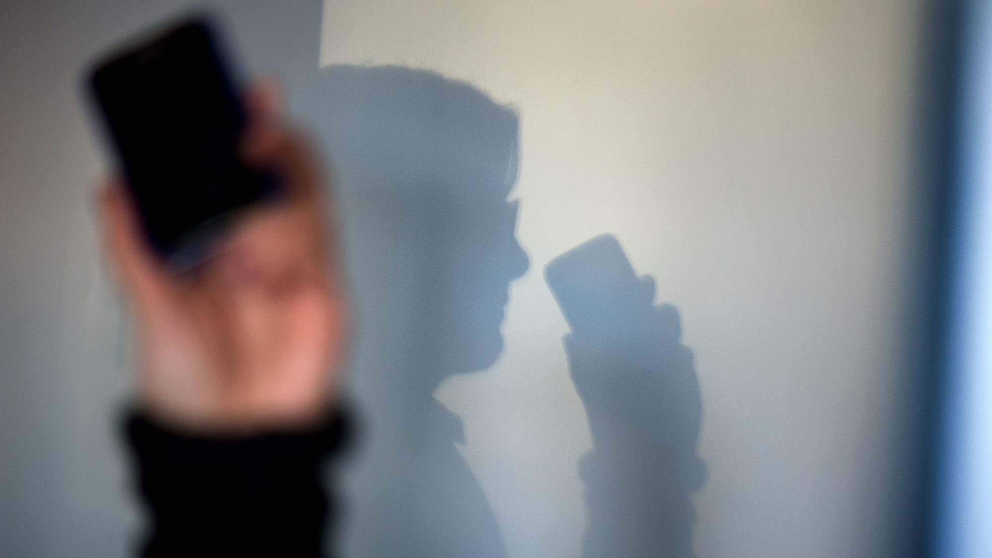 ARCHIV - 15.12.2013, Sachsen, Dresden: Eine Person telefoniert mit ihrem Mobiltelefon an der Wand zeichnet sich ihr Schatten ab. (zu dpa: «Falsche Polizistin bringt 87-Jährigen um Wertgegenstände») Foto: Arno Burgi/dpa-Zentralbild/dpa +++ dpa-Bildfunk +++