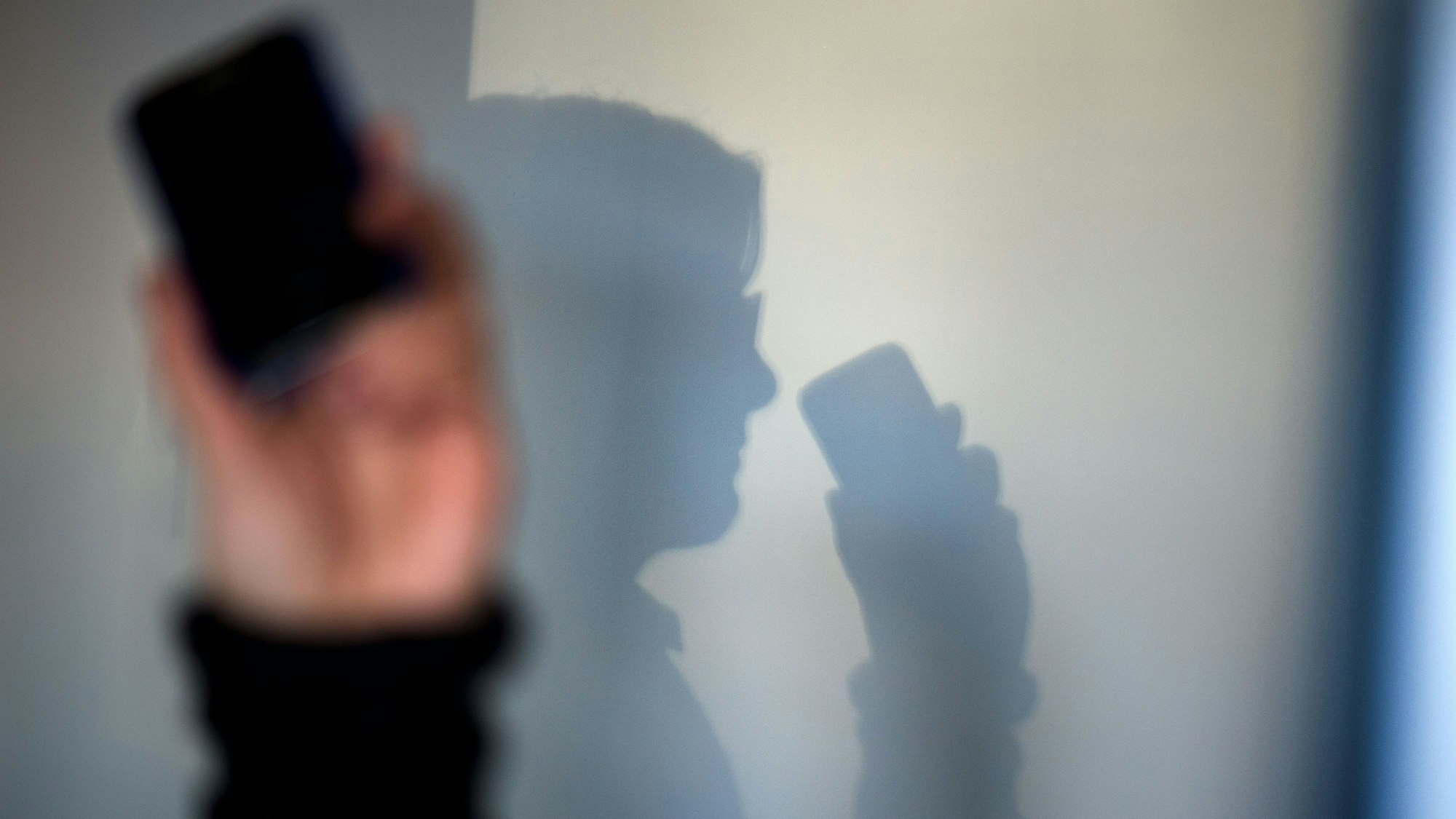 ARCHIV - 15.12.2013, Sachsen, Dresden: Eine Person telefoniert mit ihrem Mobiltelefon an der Wand zeichnet sich ihr Schatten ab. (zu dpa: «Falsche Polizistin bringt 87-Jährigen um Wertgegenstände») Foto: Arno Burgi/dpa-Zentralbild/dpa +++ dpa-Bildfunk +++