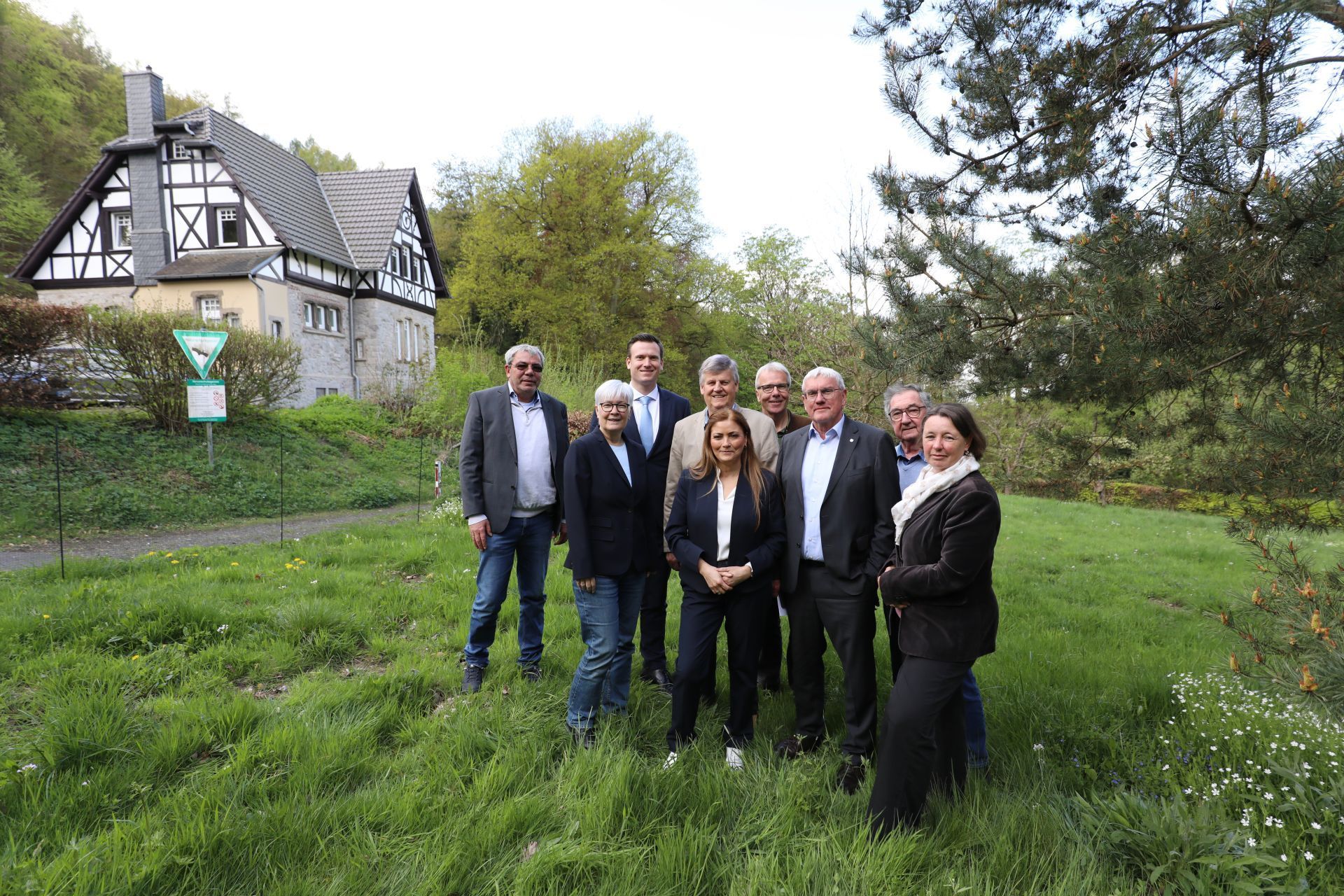 Eine Gruppe von Männern und Frauen auf einer Wiese, im Hintergrund ein Forsthaus.