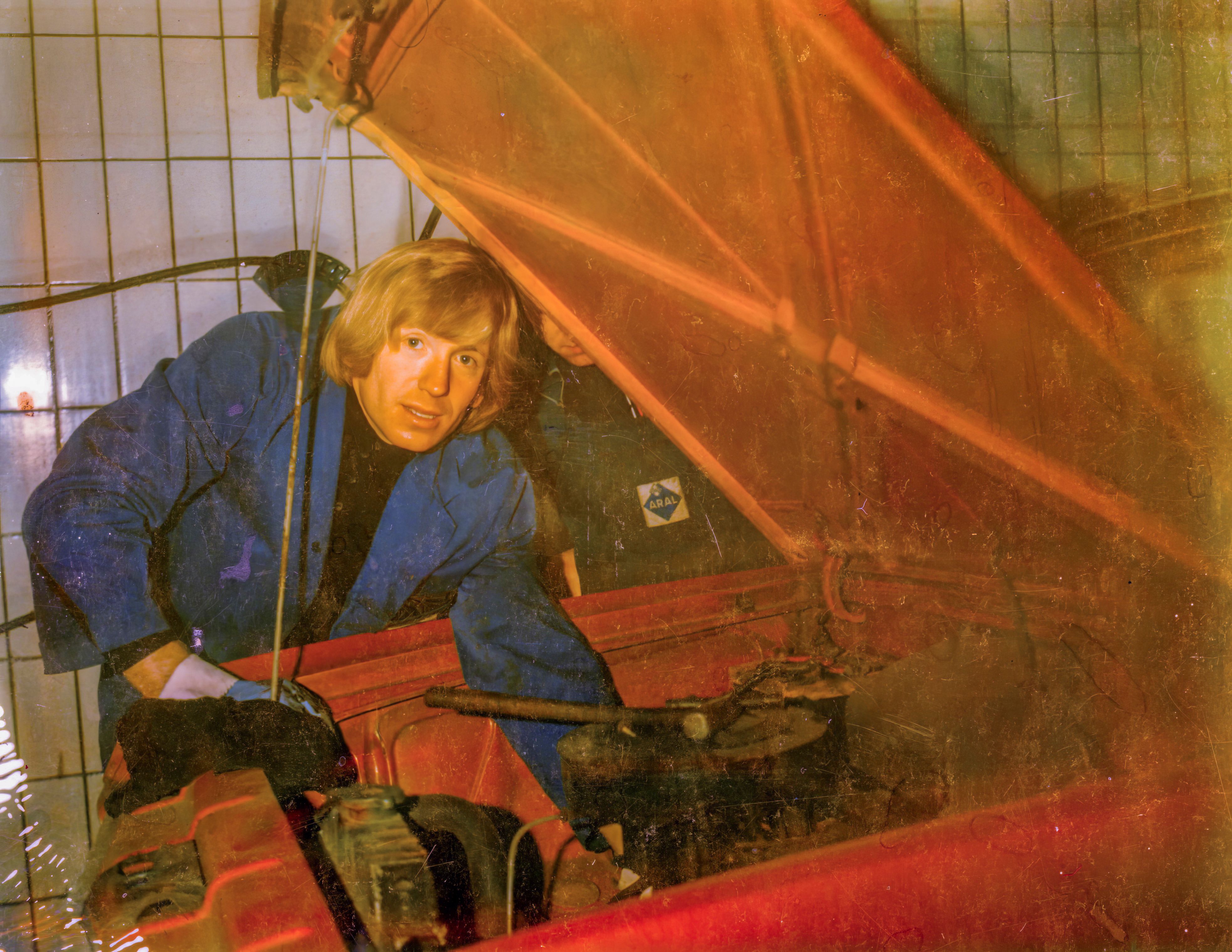 Ein Mann ist über die offene Motorhaube eines Autos gebeugt.