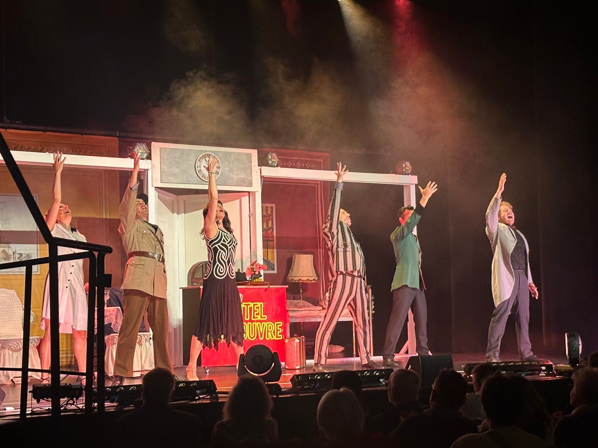 Zu sehen ist eine Theater-Besetzung auf der Bühne. Sie recken jeweils ihren linken Arm in die Höhe in Richtung Scheinwerfer.