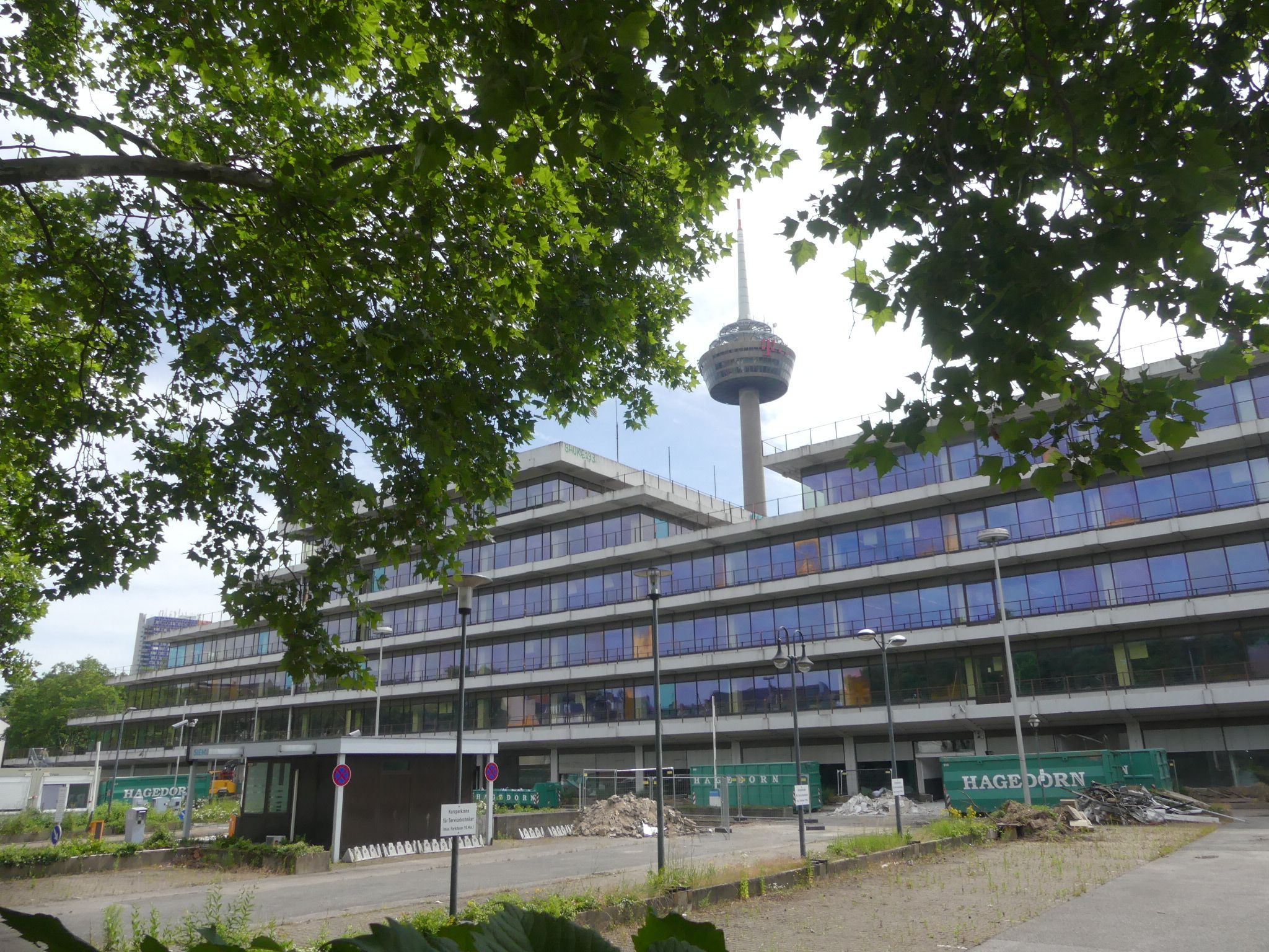 Ein mehrgeschossiges Bürogebäude ist zu sehen, im Hintergrund ragt der Colonius in die Höhe.