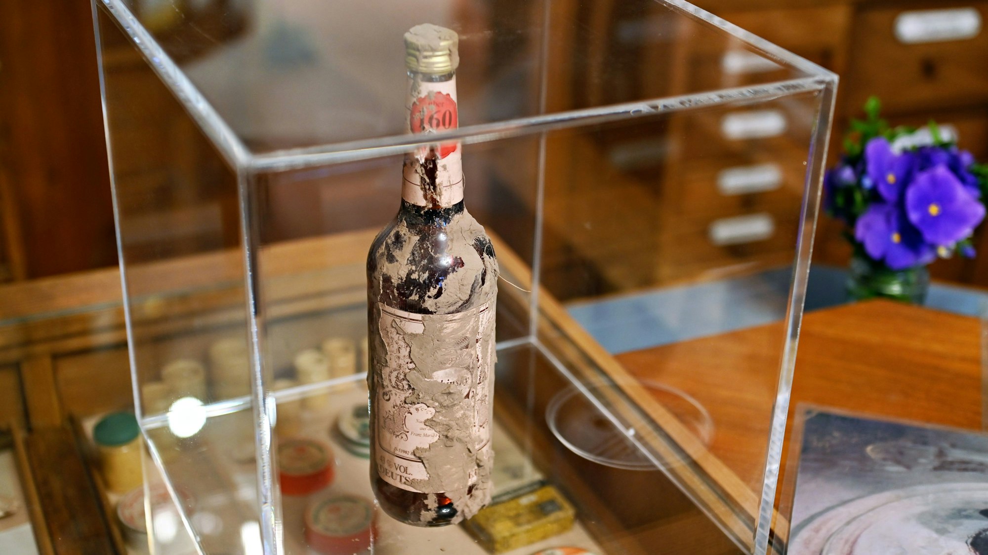 In einer Glasvitrine wird eine schlammverschmierte Flasche ausgestellt.