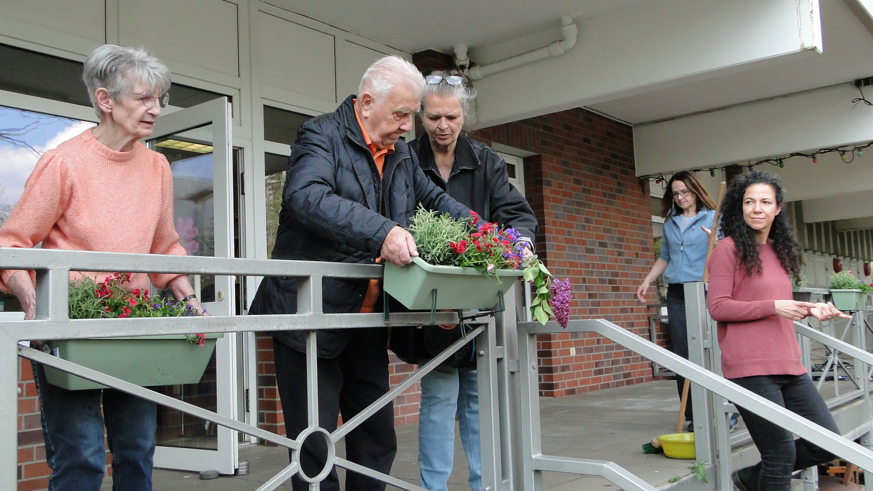 Fünf Personen verschiedenen Alters beim Aufhängen von Blumenkästen. Auch die Blumenkästen an der Terrasse wurden beim ersten Treffen des Gartenprojekts neu bestückt.