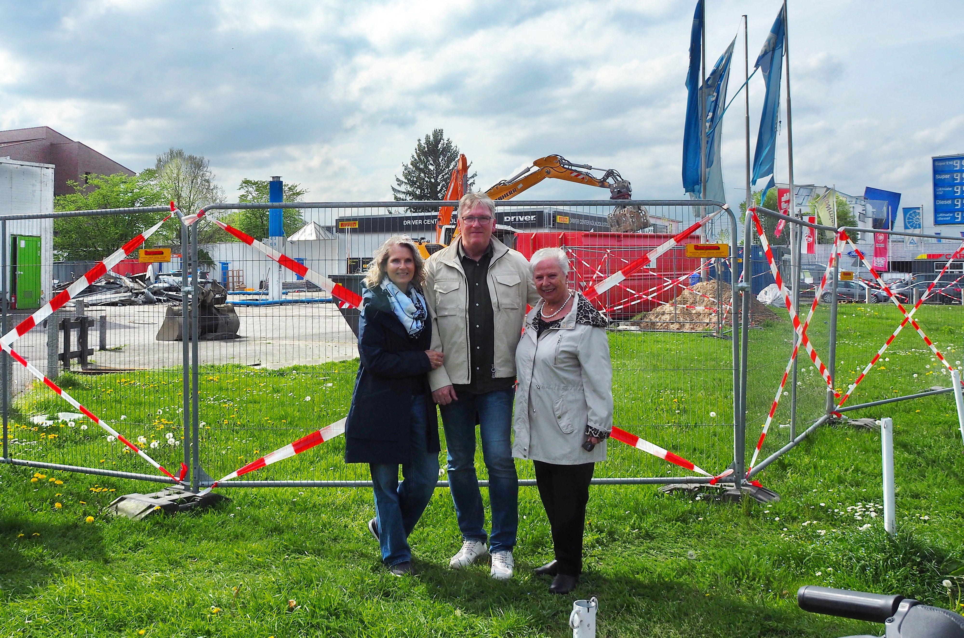 Ein Mann steht mit seiner Frau und seiner Mutter vor dem Bauzaun, hinter der die Aral-Tankstelle in Zollstock abgerissen wird.