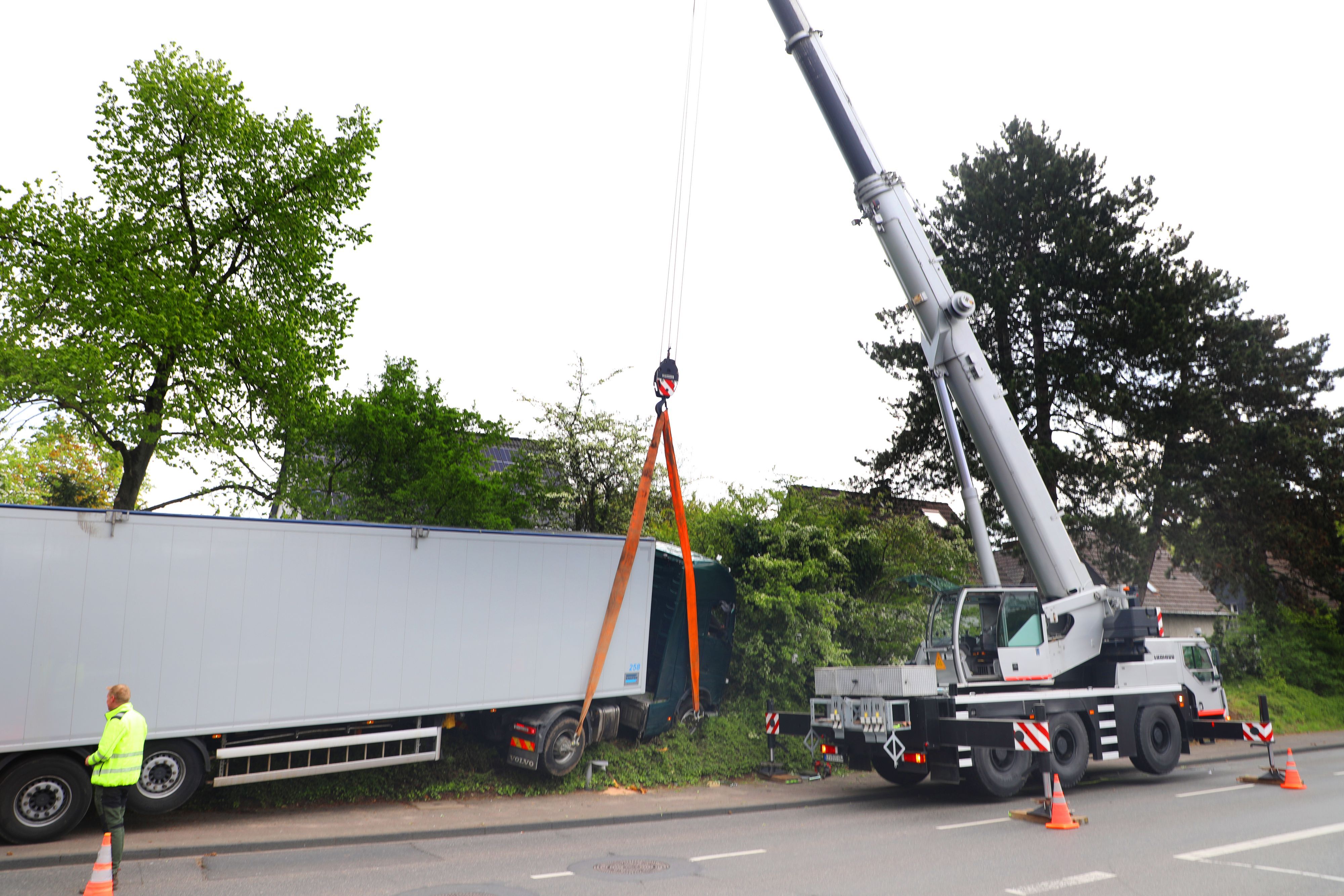 Ein Autokran hebt einen Sattelzug aus einer Böschung.