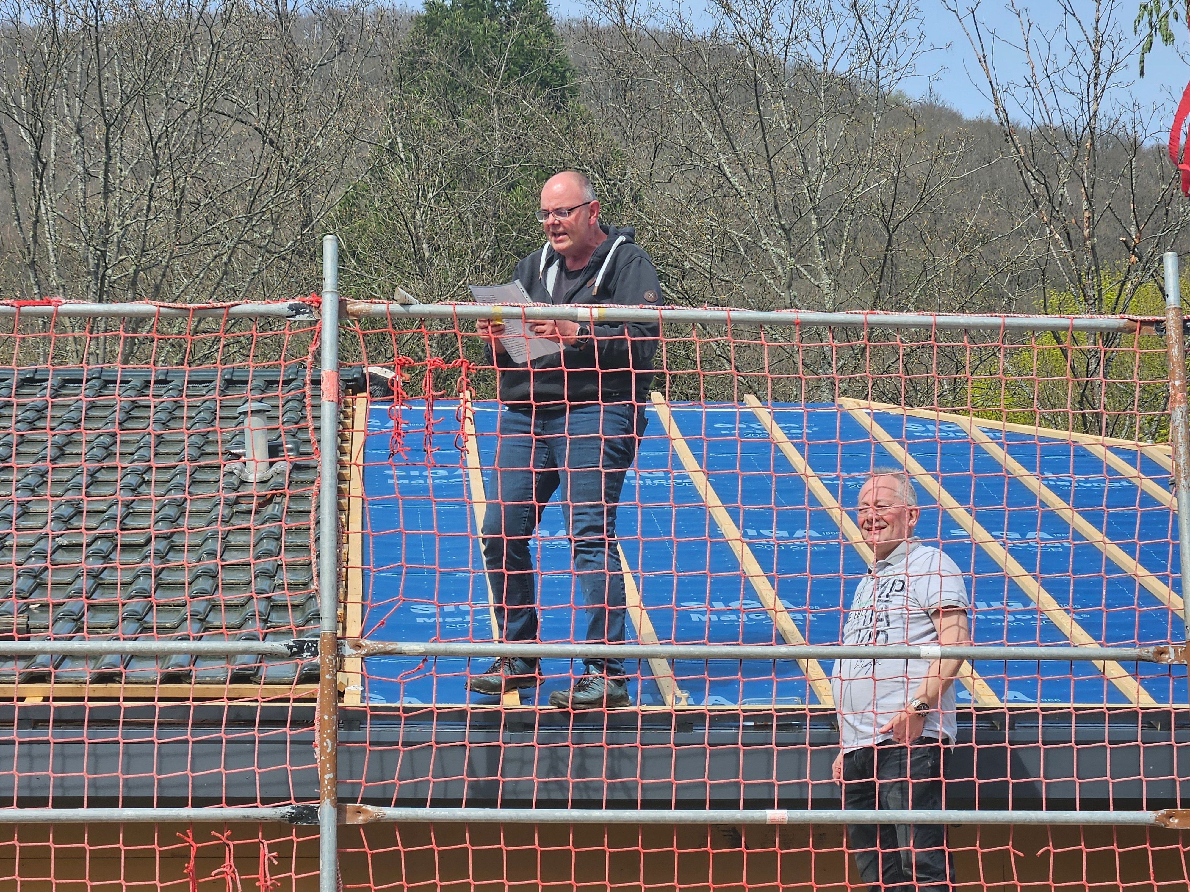 Ein Mann steht auf einem Dachsparren, ein anderer daneben auf einem Gerüst.