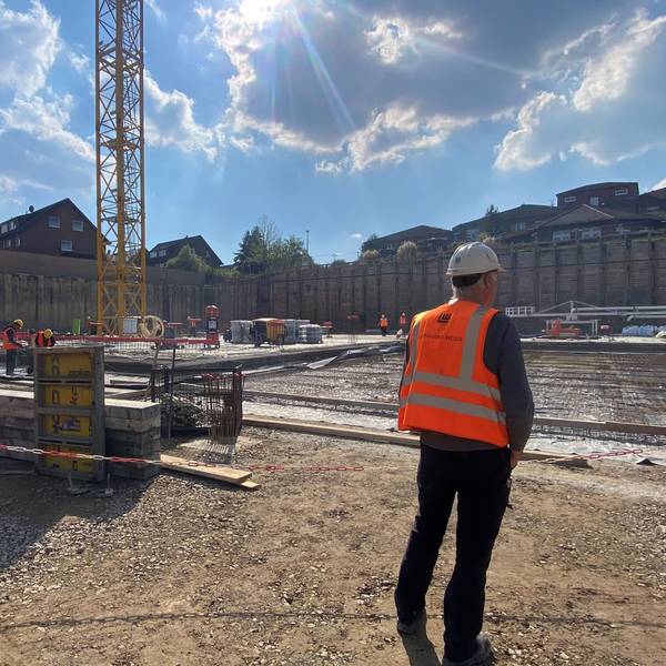 Zu sehen ist die Baustelle, im Vordergrund steht ein Arbeiter.