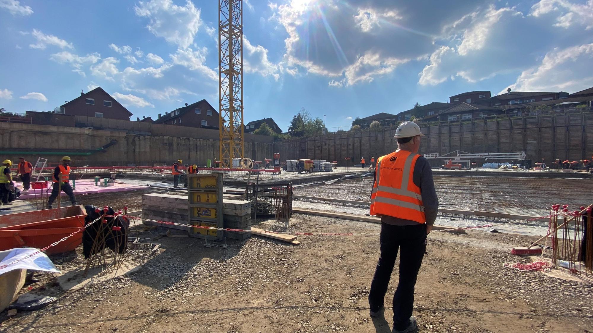 Zu sehen ist die Baustelle, im Vordergrund steht ein Arbeiter.