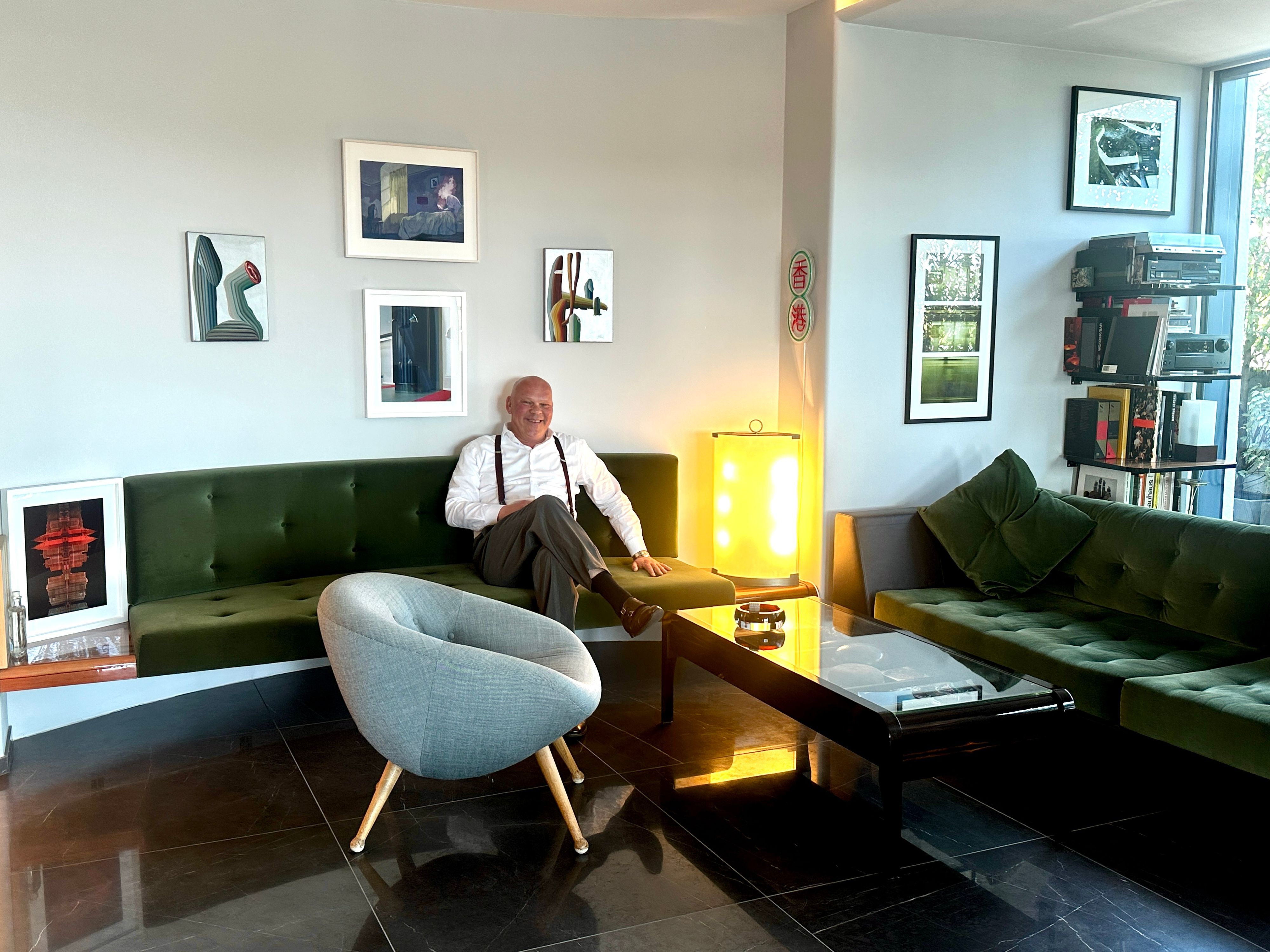 Ein Mann in weißem Hemd und Hosenträgern sitzt auf einem grünen Sofa.