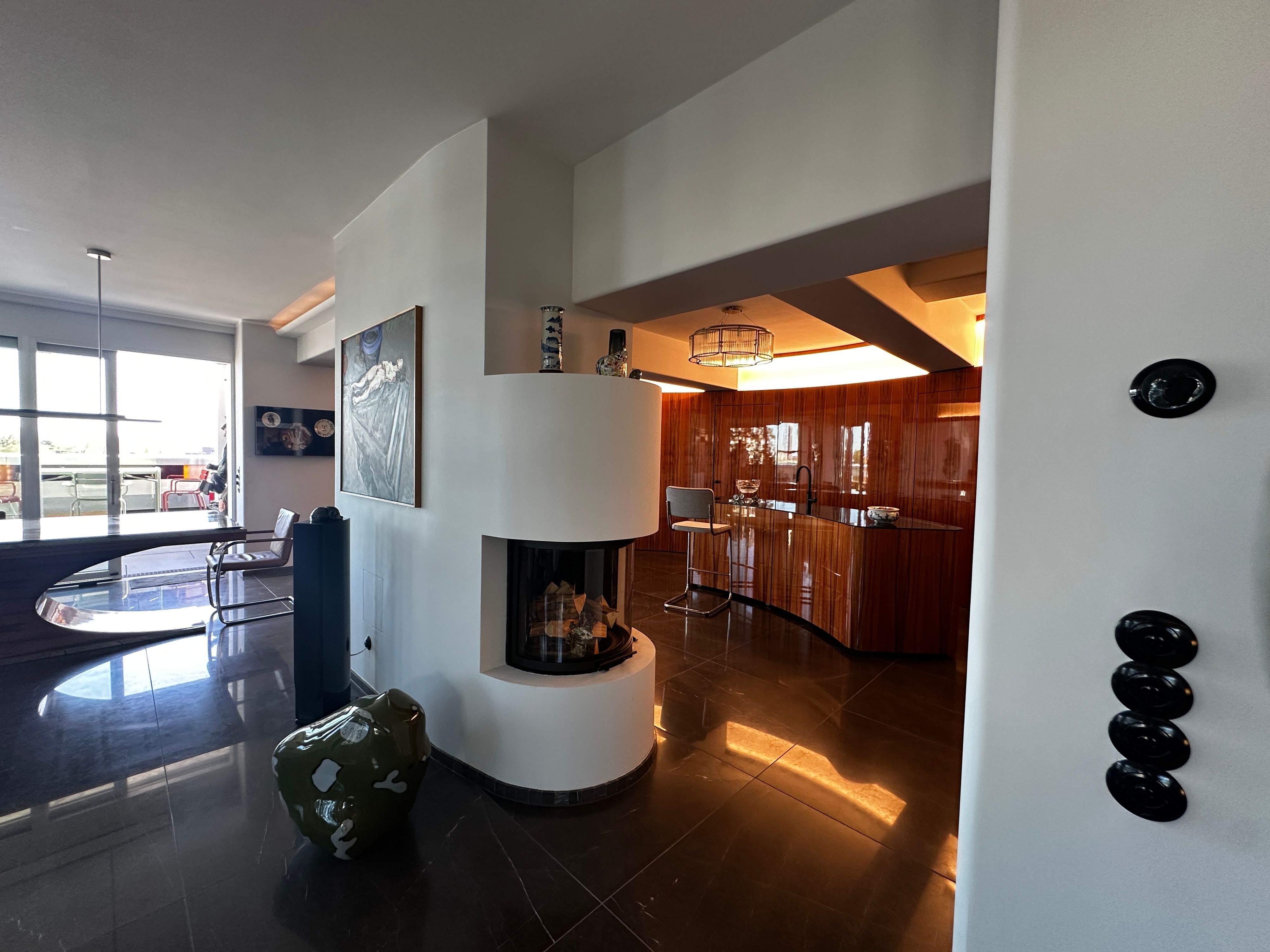 Blick in einen hochwertigen Innenraum, ein halbrunder Kachelofen trennt einen Barbereich vom Essbereich.