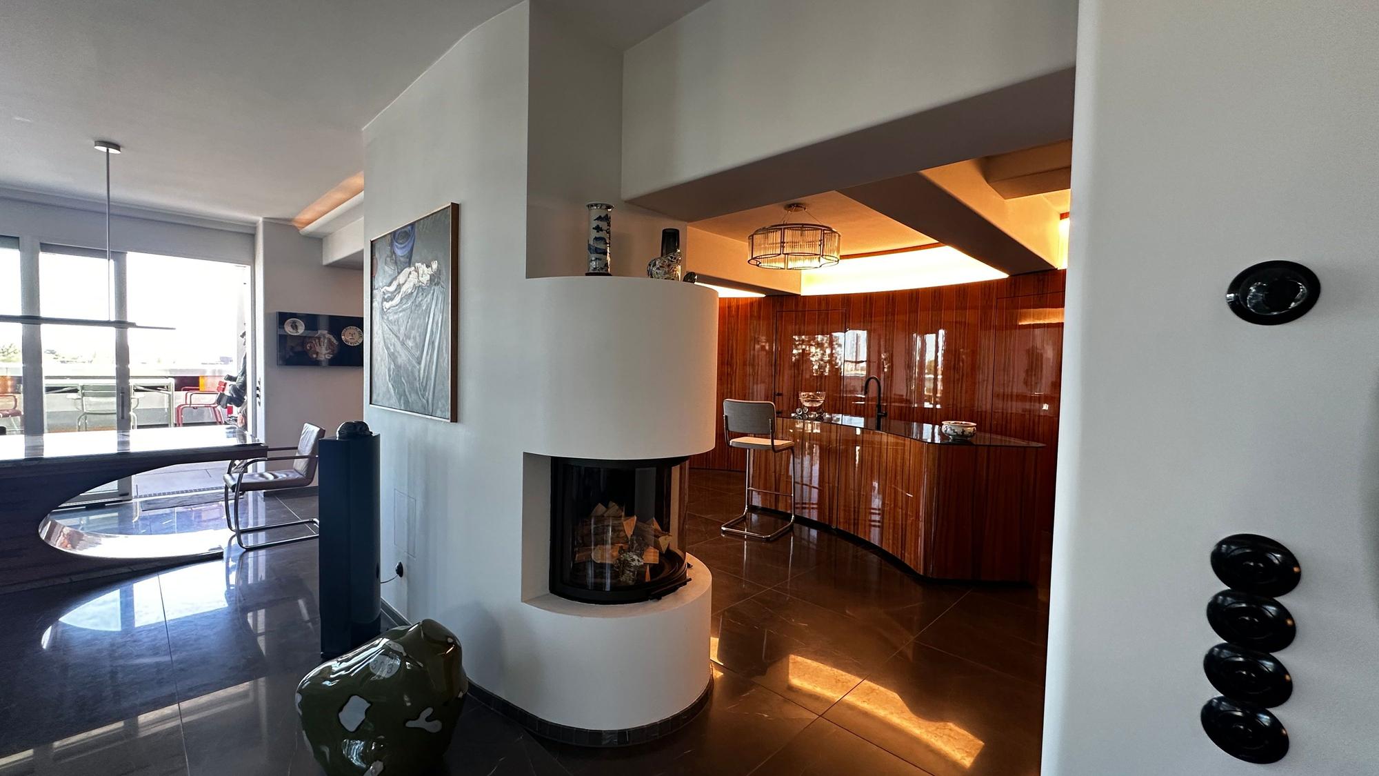 Blick in einen hochwertigen Innenraum, ein halbrunder Kachelofen trennt einen Barbereich vom Essbereich.