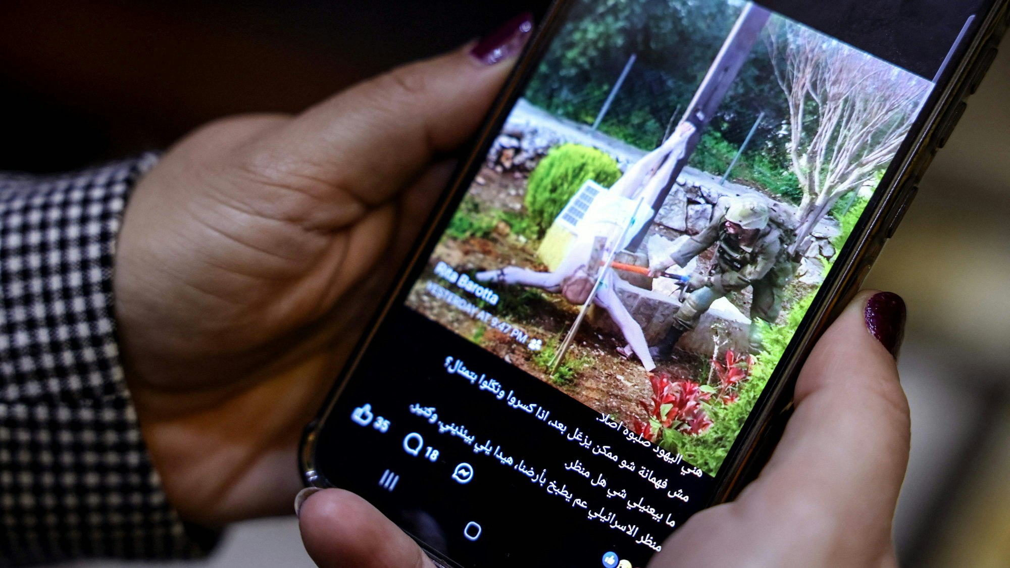 Eine Frau sieht sich auf ihrem Handy einen Social-Media-Beitrag an, der ein Bild zeigt, auf dem offenbar ein israelischer Soldat im Südlibanon auf eine Jesus-Christus-Statue einschlägt.