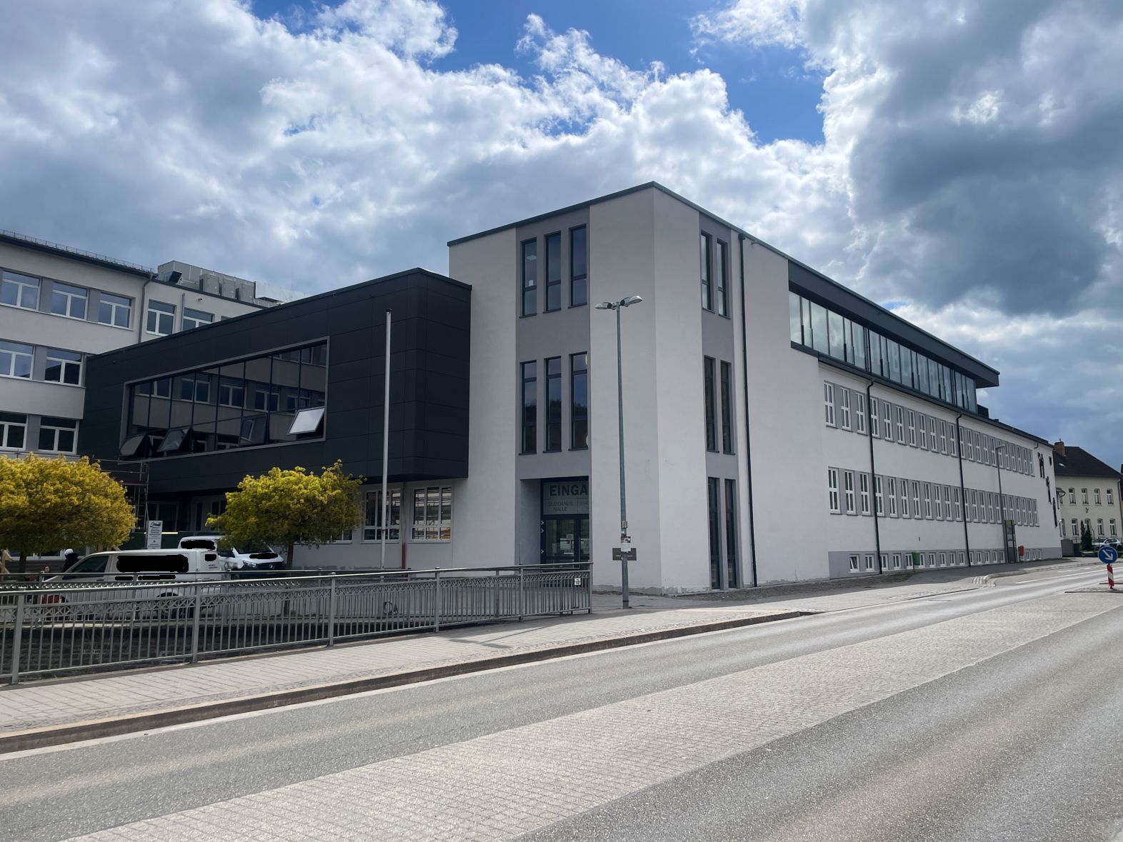 Die dunkle Fassade des neuen Gebäudeteils hebt sich von der hellen Front der Schule ab.