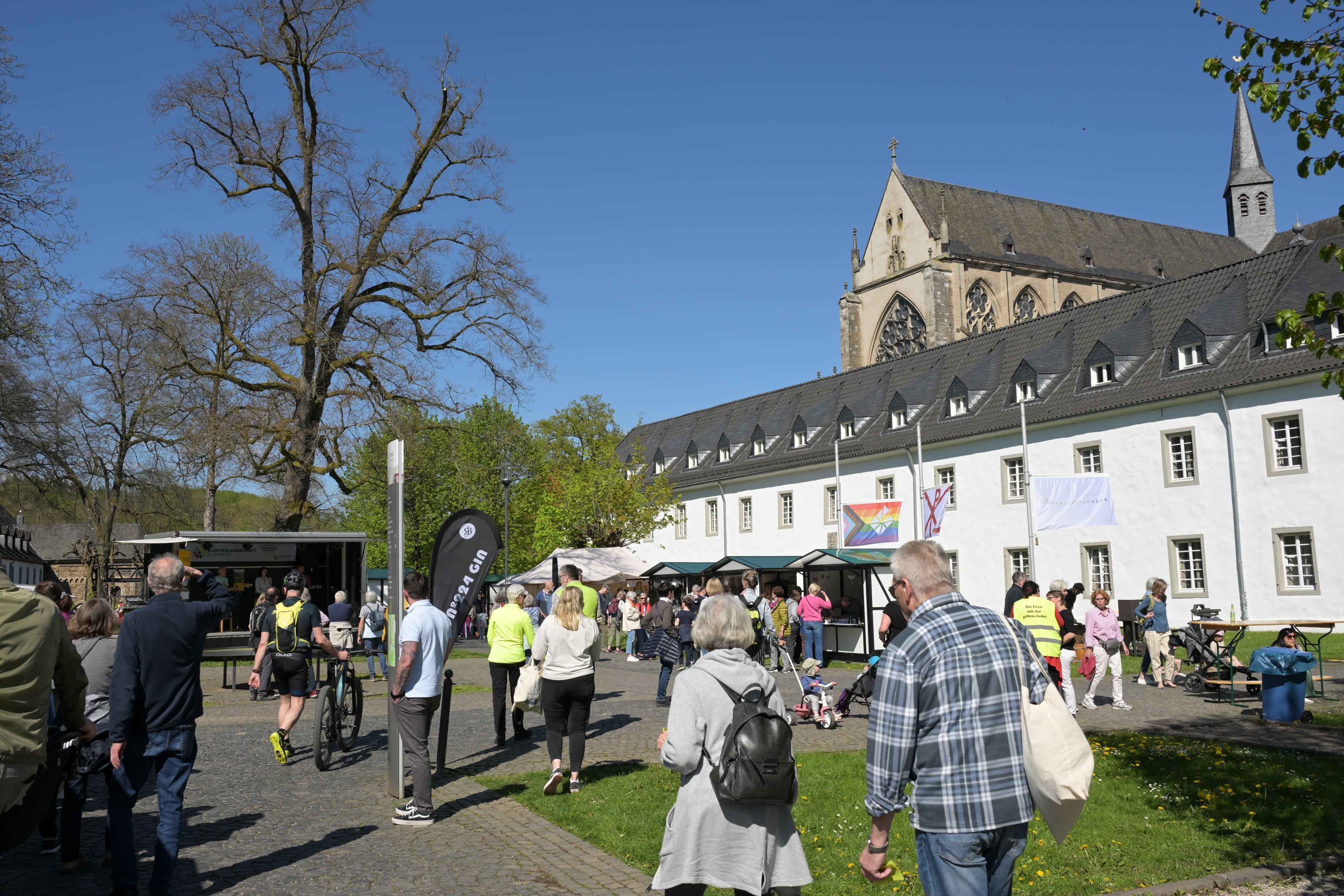 Der Altenberger Dom, davor das gebäude der Jugendbildungsstätte haus Altenberg und viele Menschen an Ständen an einem sommerlichen Tag.